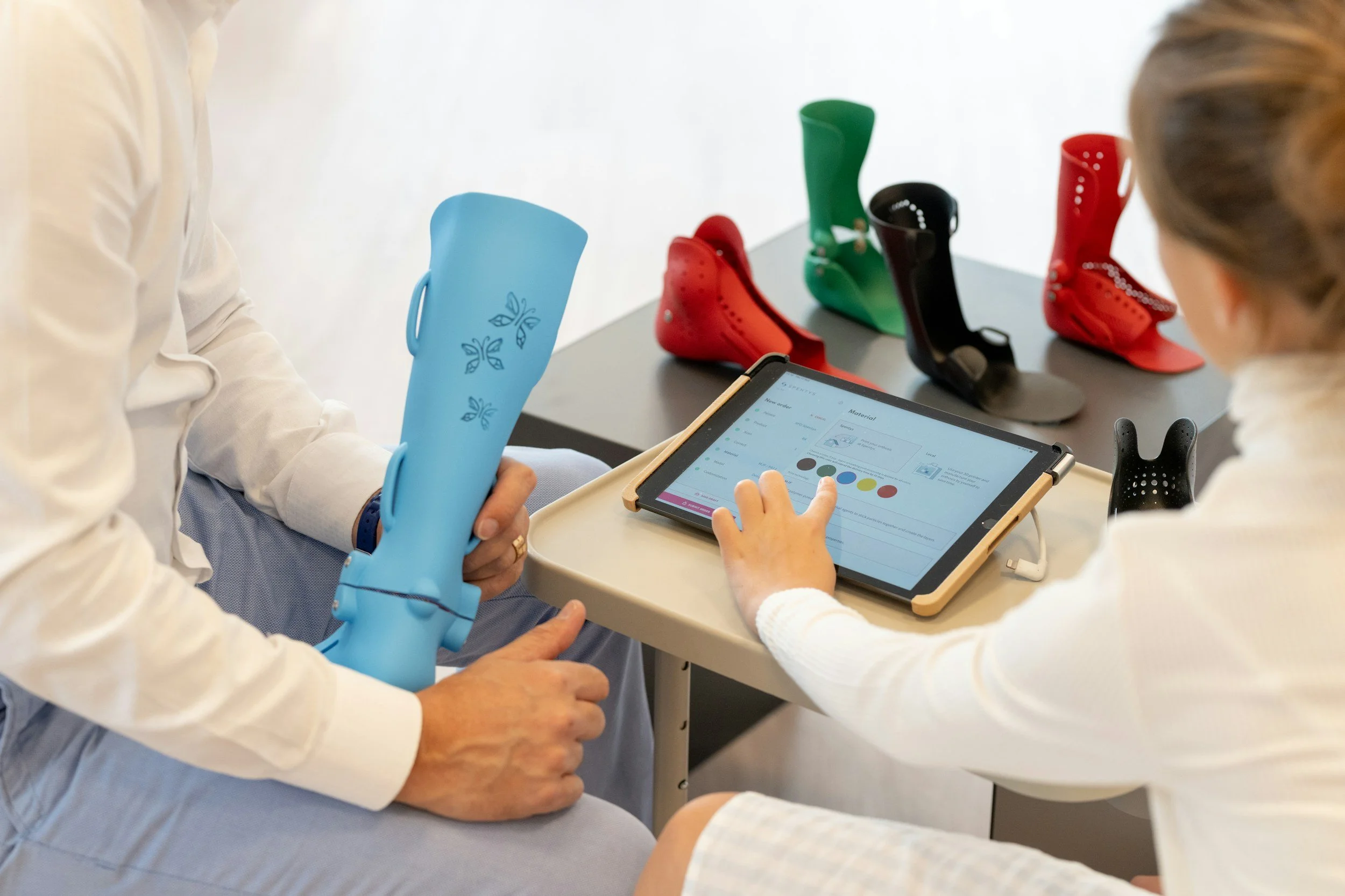 People working with prosthetic limbs and a tablet displaying material options on a white table.