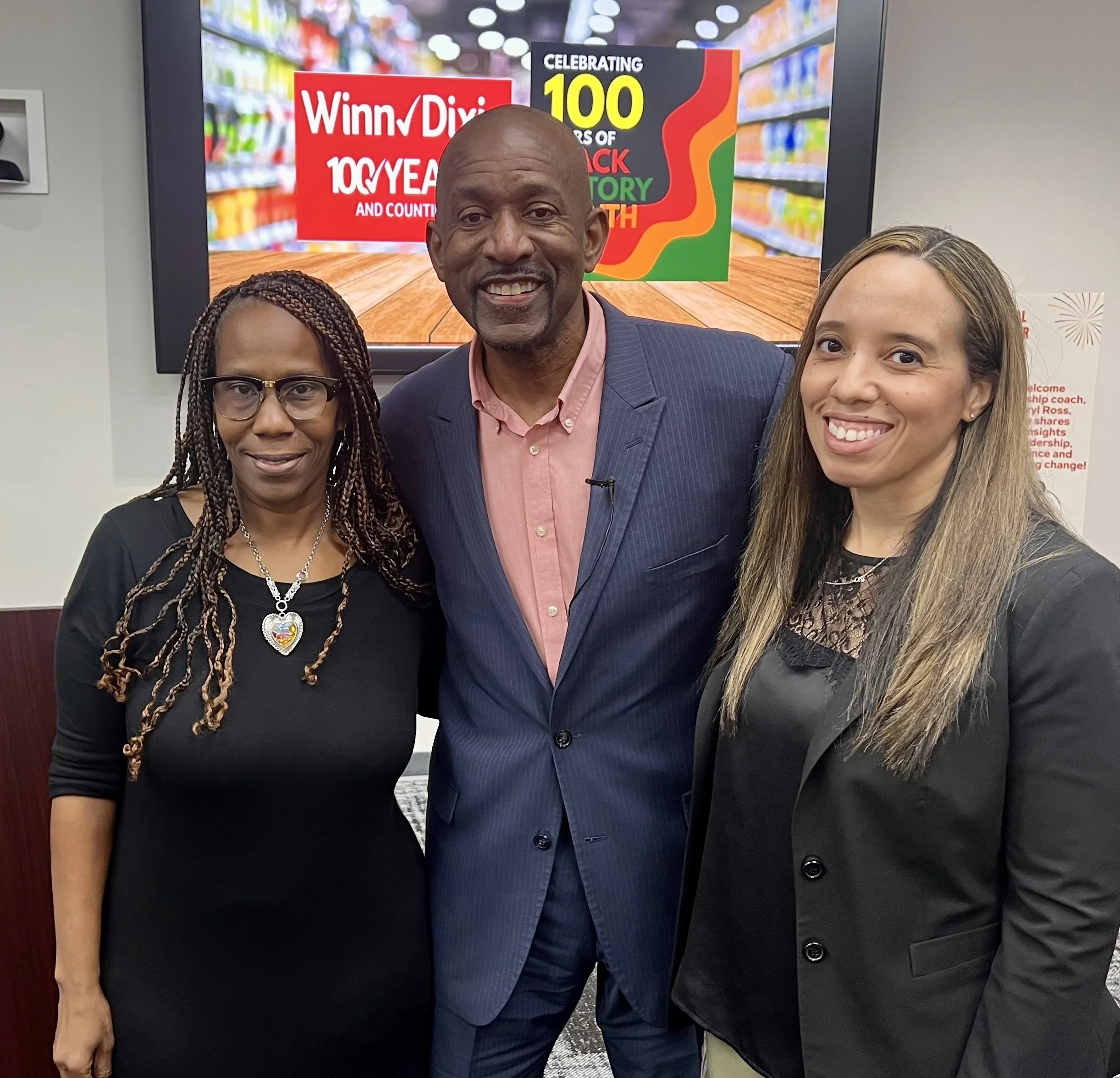 Darryl Ross with leadership from Winn-Dixie celebrating 100 years of the Winn-Dixie grocery store chain, with shelves of products visible in the background.