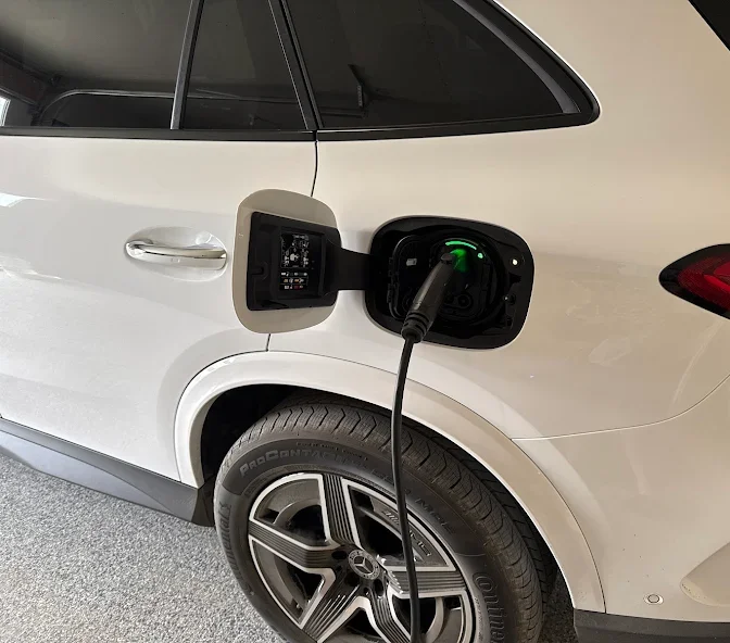 Electric vehicle charging port with a charger plugged in on a white SUV.