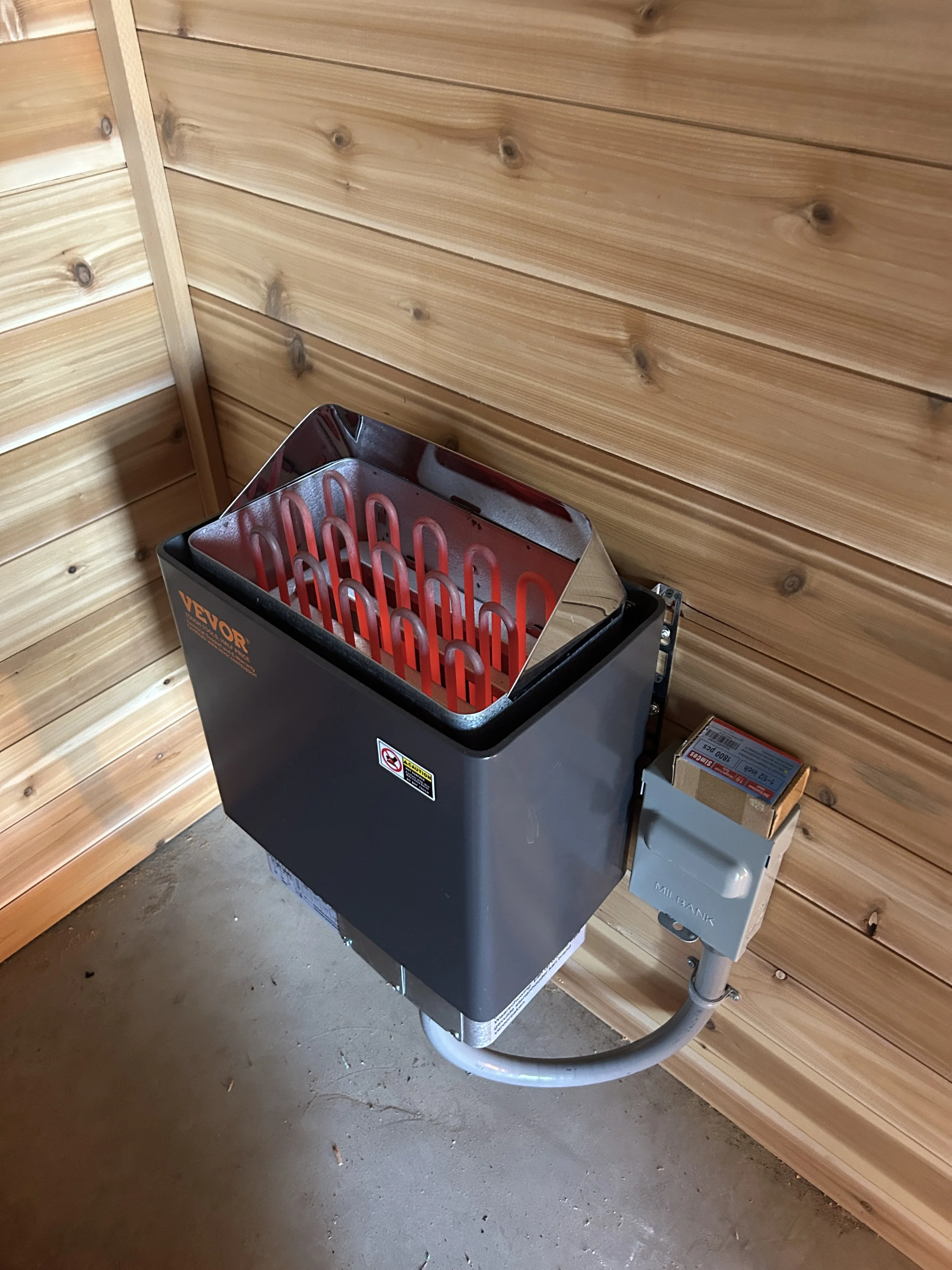 A wood-paneled wall with a sauna heater and a metal box attached to the wall.