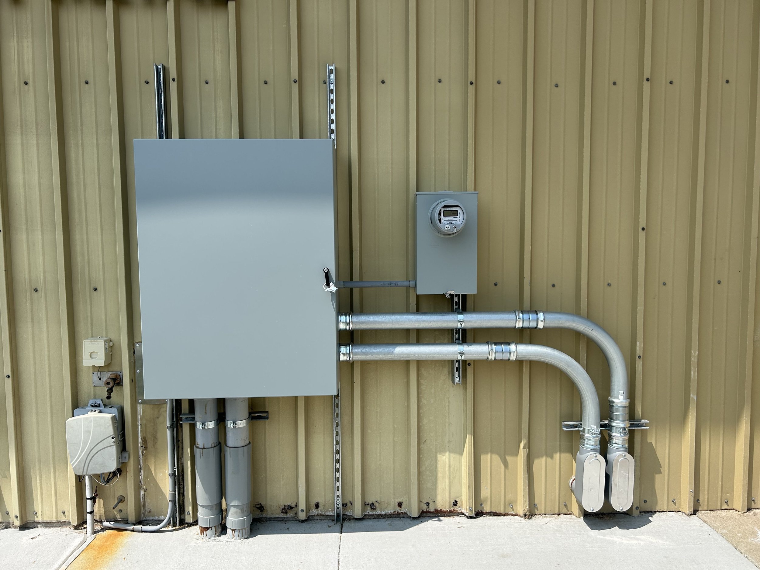 Electrical and plumbing equipment mounted on a yellow corrugated metal wall.