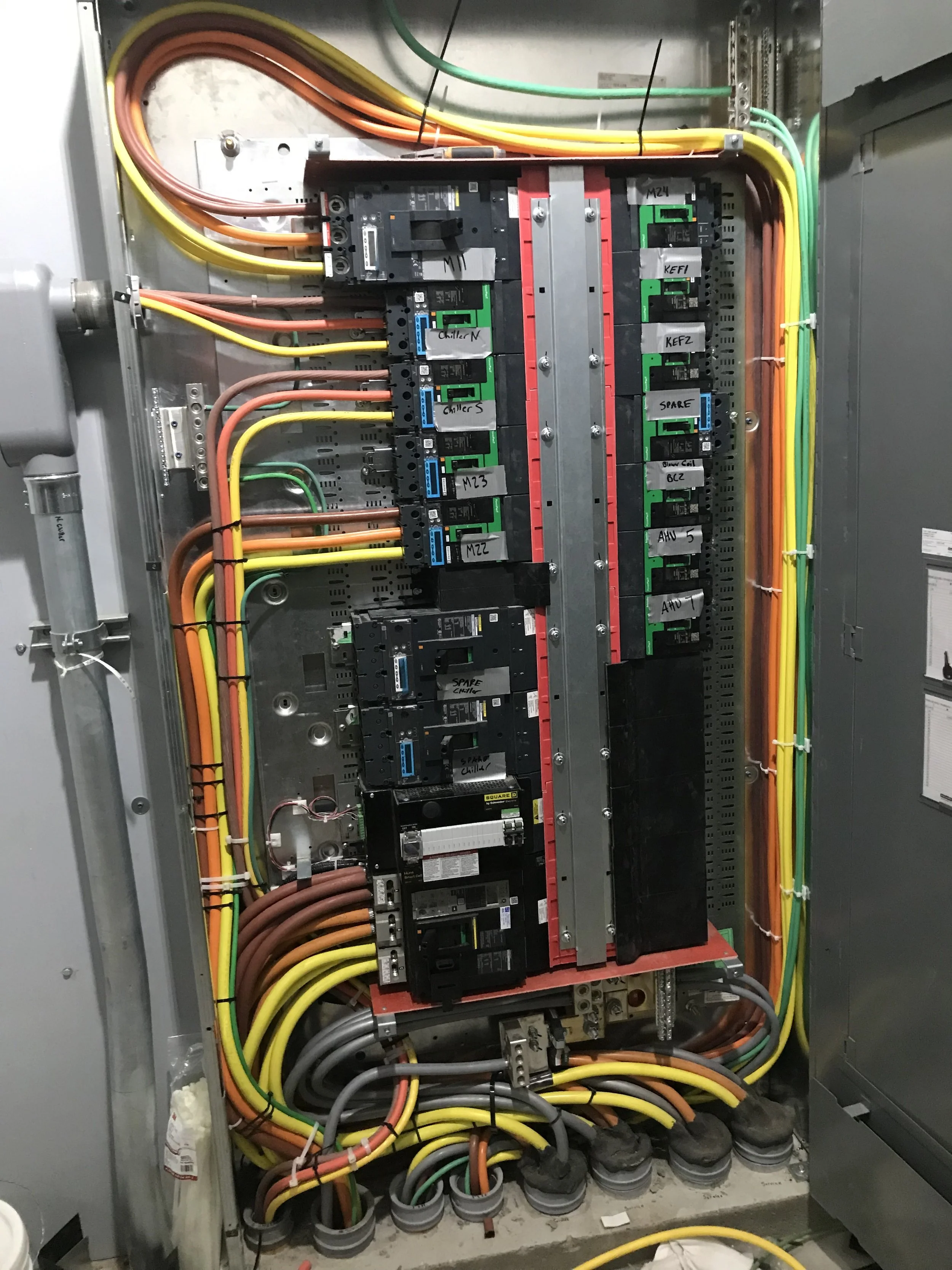 Electrical panel with various wires and circuit breakers, labeled with different categories, installed inside a metal box.
