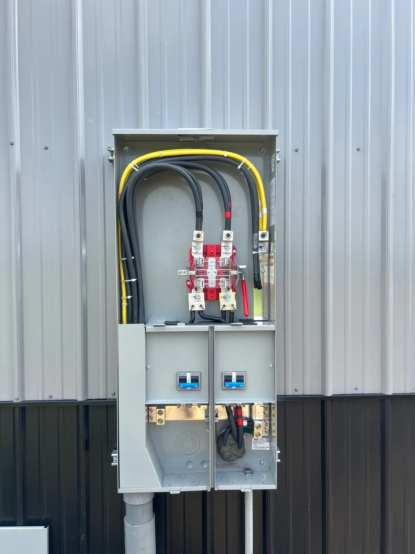 Electrical panel with black and yellow wires, mounted on a metal wall, with electrical meters at the bottom.