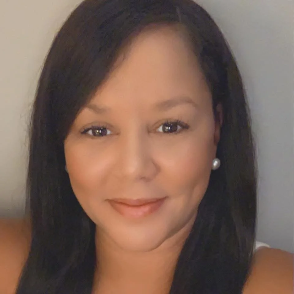 Close-up headshot of a woman with dark hair, light makeup, pearl earrings, smiling gently, the founder of Inspire Breathwork, Audrey Cook.