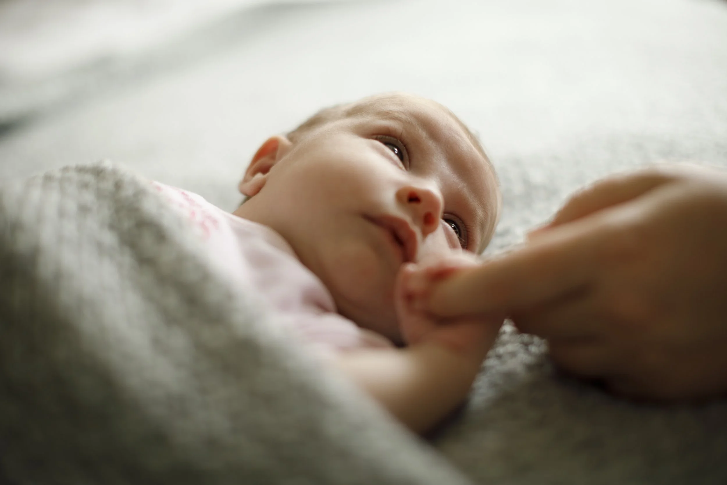 Close-up of a newborn baby lying on a soft surface, looking to the side with wide eyes.