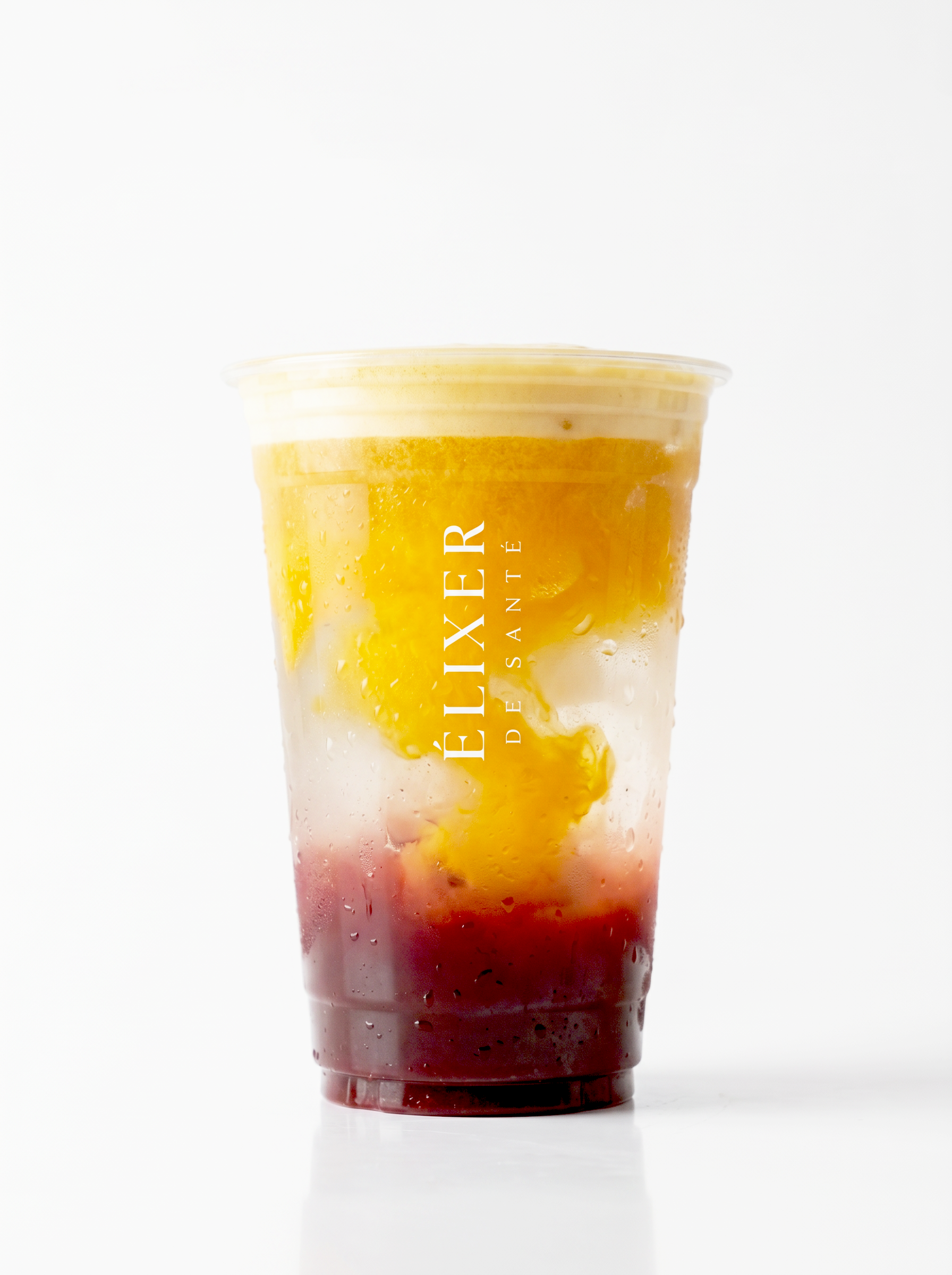 A tall transparent plastic cup filled with a layered colorful drink, with condensation on the outside, and the word 'FÉLIXIER' written vertically in white letters.