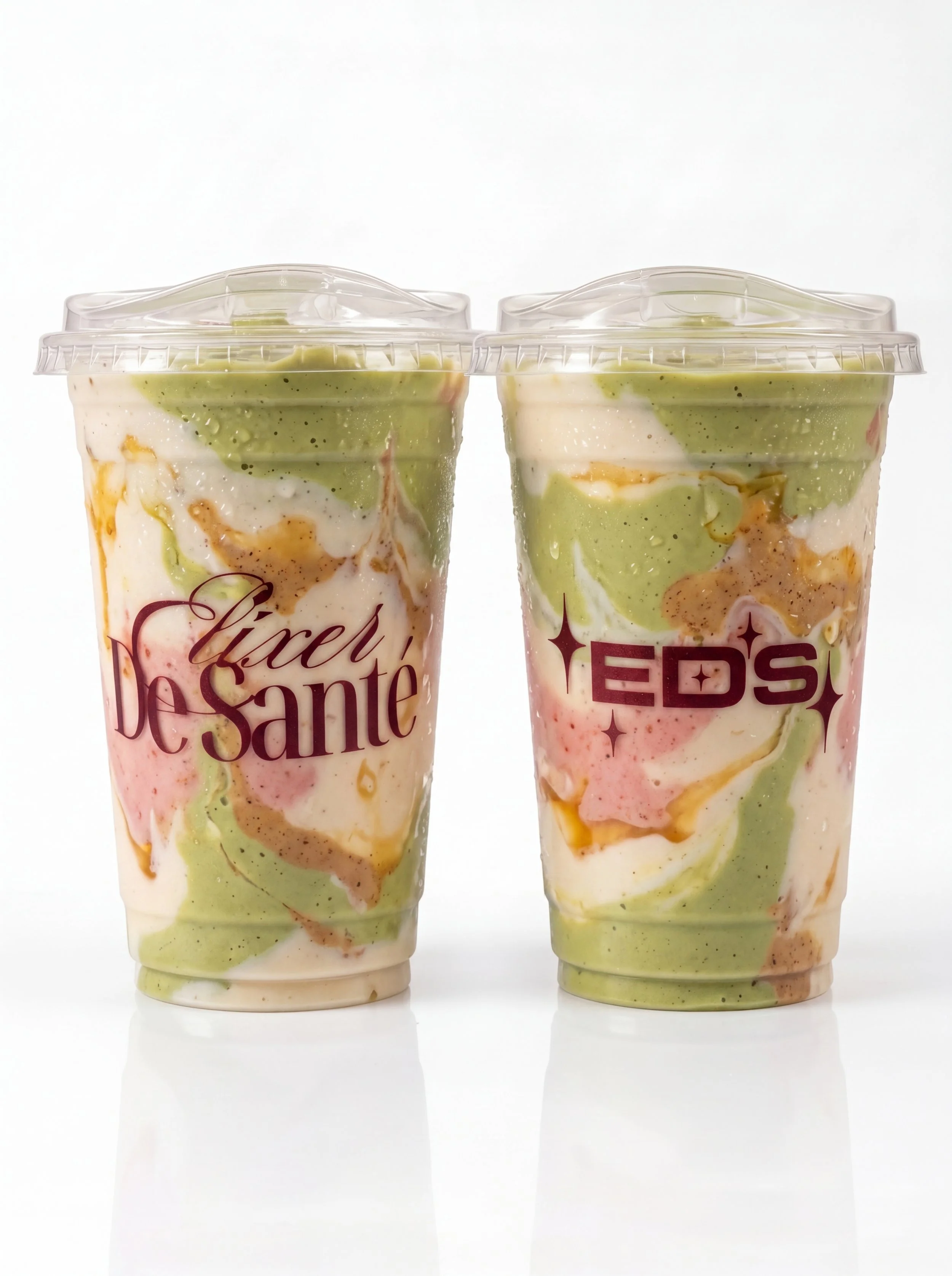 Two cups of freshly made fruit juice in clear plastic cups with dome lids, showcasing vibrant natural colors from fresh fruits. Premium handcrafted beverages from Elixer De Sante, made with wholesome ingredients and perfect for a refreshing, healthy