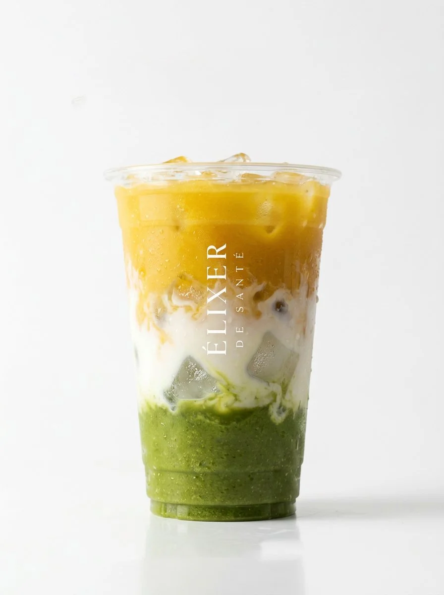 Layered matcha, vanilla, and mango smoothie A handcrafted layered iced beverage in a clear plastic cup branded with the Elixer De Sante logo, featuring distinct layers of green, white, and golden yellow, displayed against a clean white background.