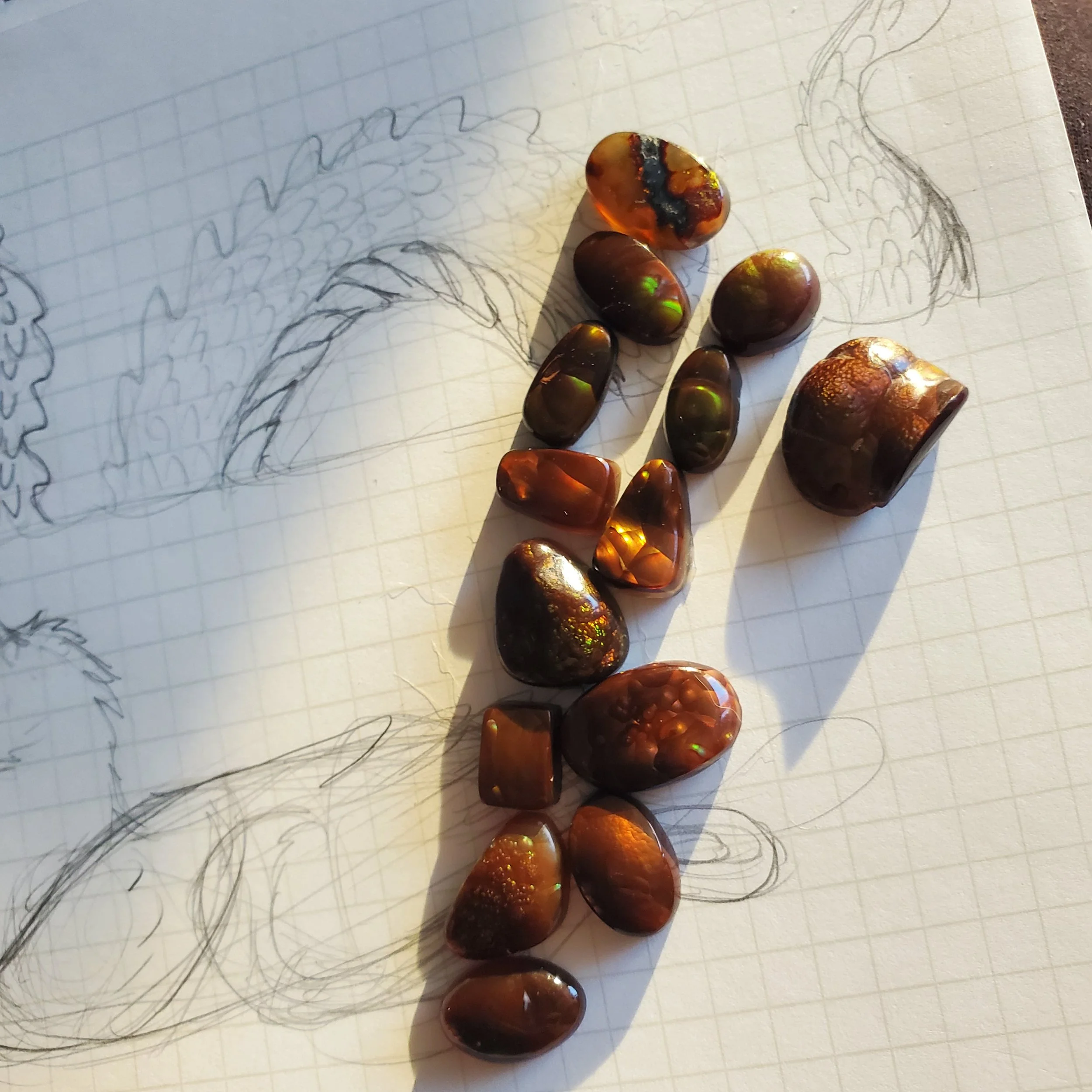 Multiple polished fire agate stones of various sizes and shapes placed on a piece of paper with a hand-drawn sketch of a dragon, on a textured surface.