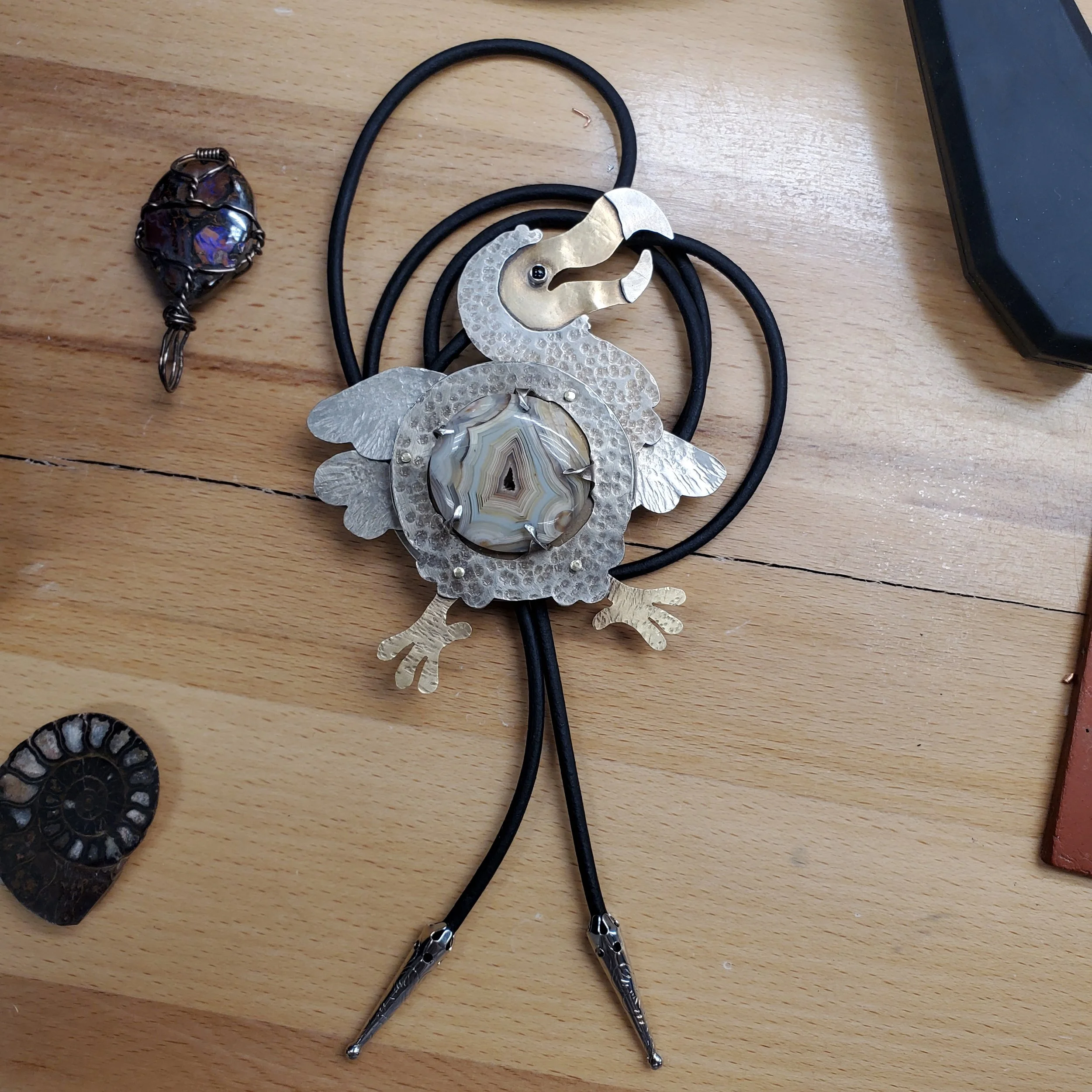 An assortment of jewelry and accessories on a wooden surface, a dodo bird bolo tie and other small objects.
