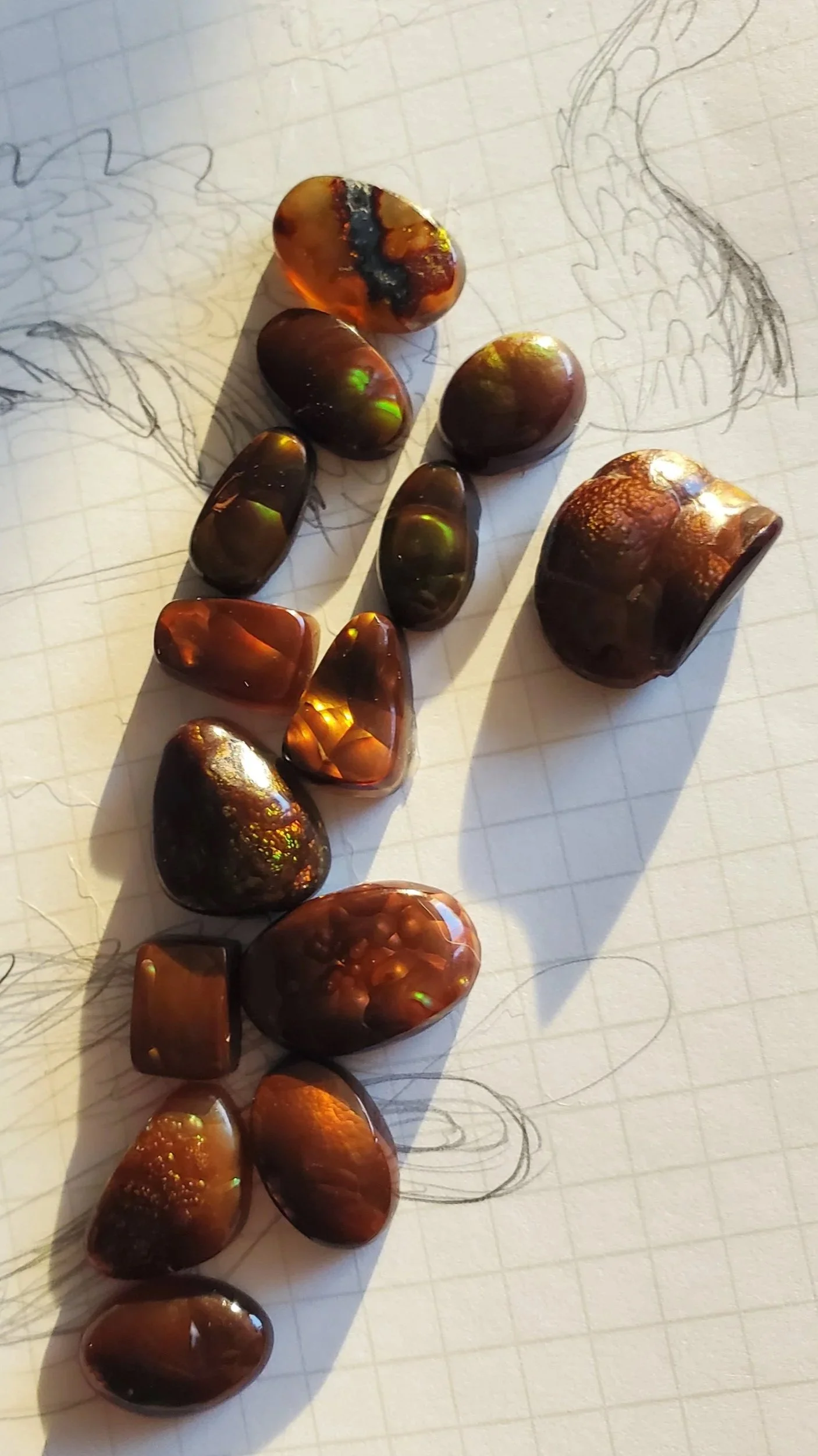 Several polished fire agate with varying shapes and sizes on graph paper with pencil sketches of dragons..
