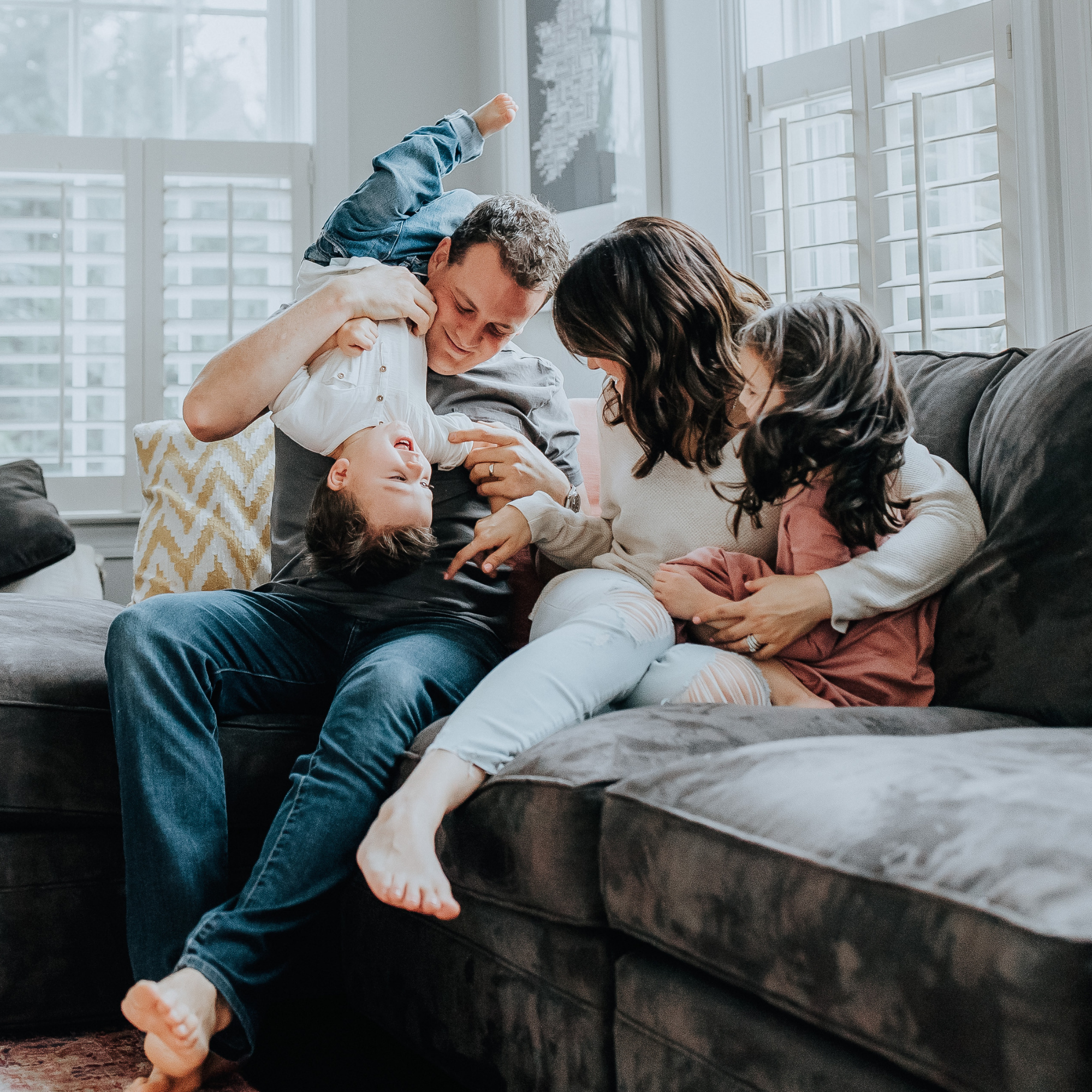 Family playing on the floor at home, with a father and mother and their young children engaging in playful activity.