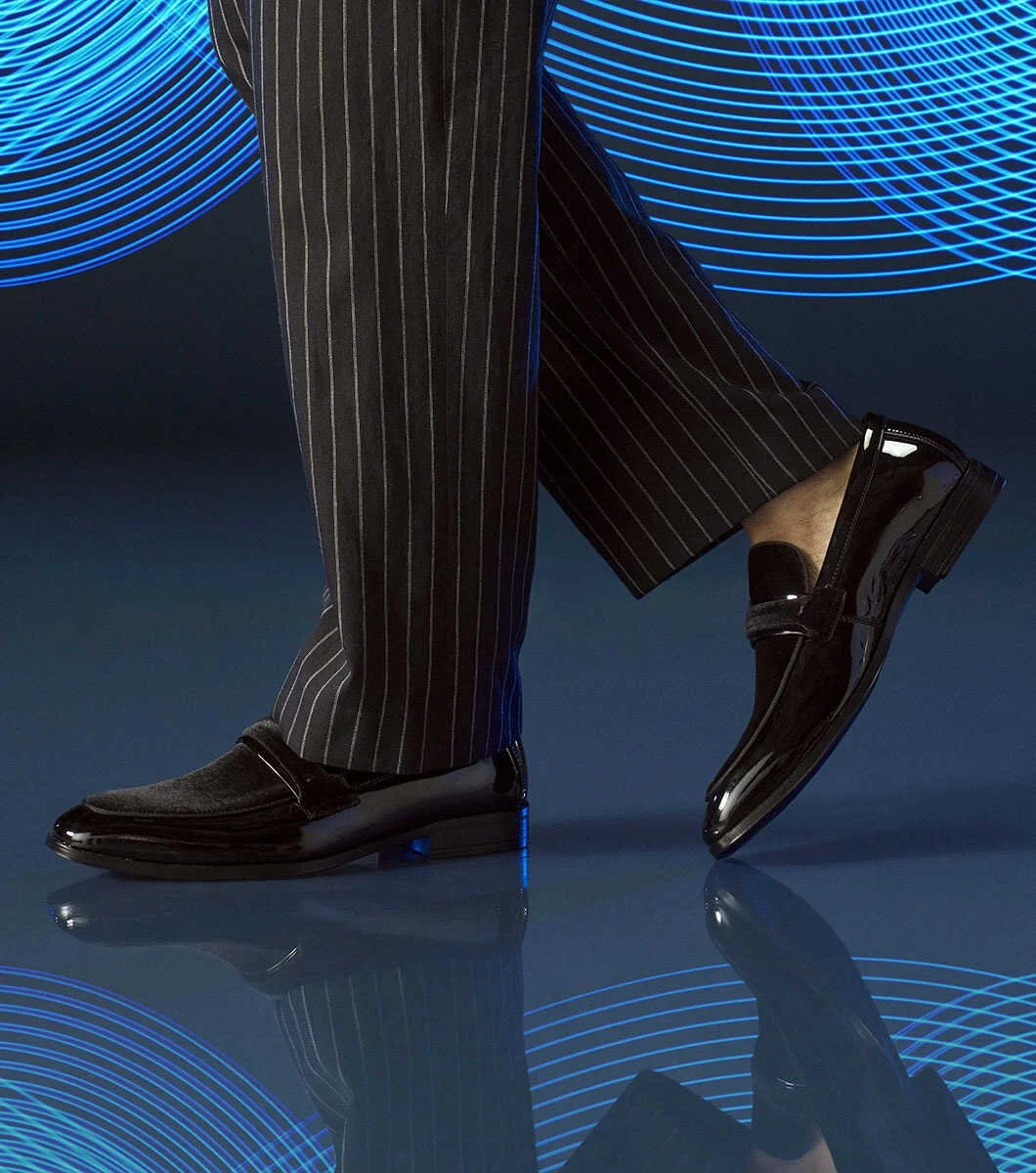 Close-up of a person wearing black patent leather dress shoes and pinstripe trousers against a blue background with digital wave patterns.