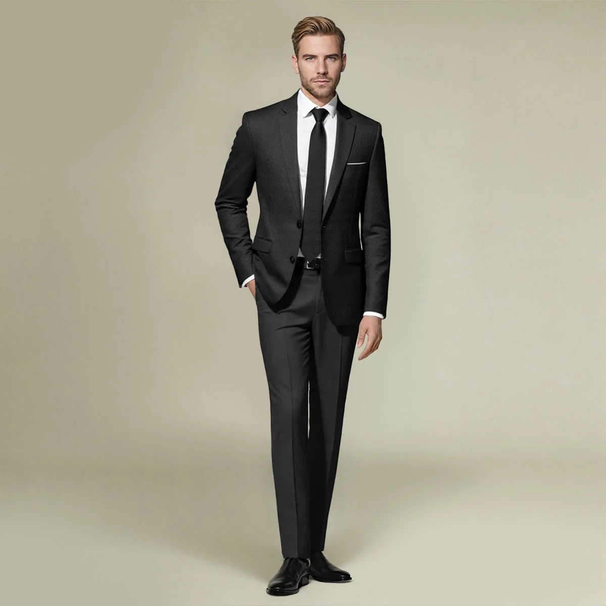 A man in a black suit, white shirt, black tie, and dress shoes standing with one hand in his pocket against a neutral background.