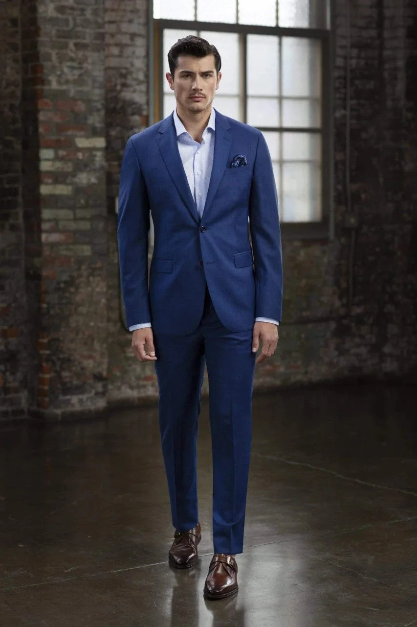 A man in a blue suit walking in an industrial-style room with exposed brick walls and large windows.