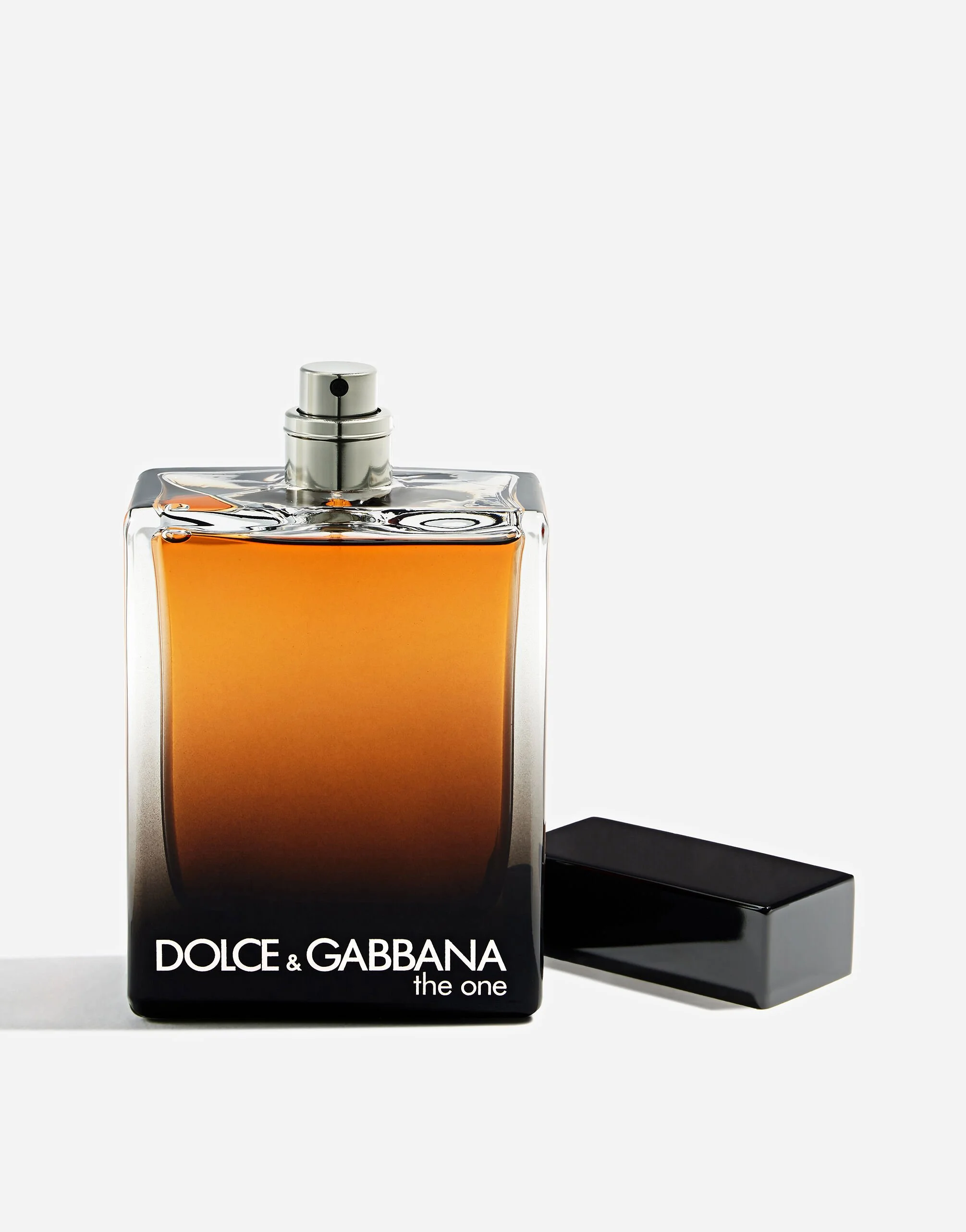 A bottle of Dolce & Gabbana the one perfume with a black box beside it, with a silver spray nozzle and orange liquid inside, set against a white background.