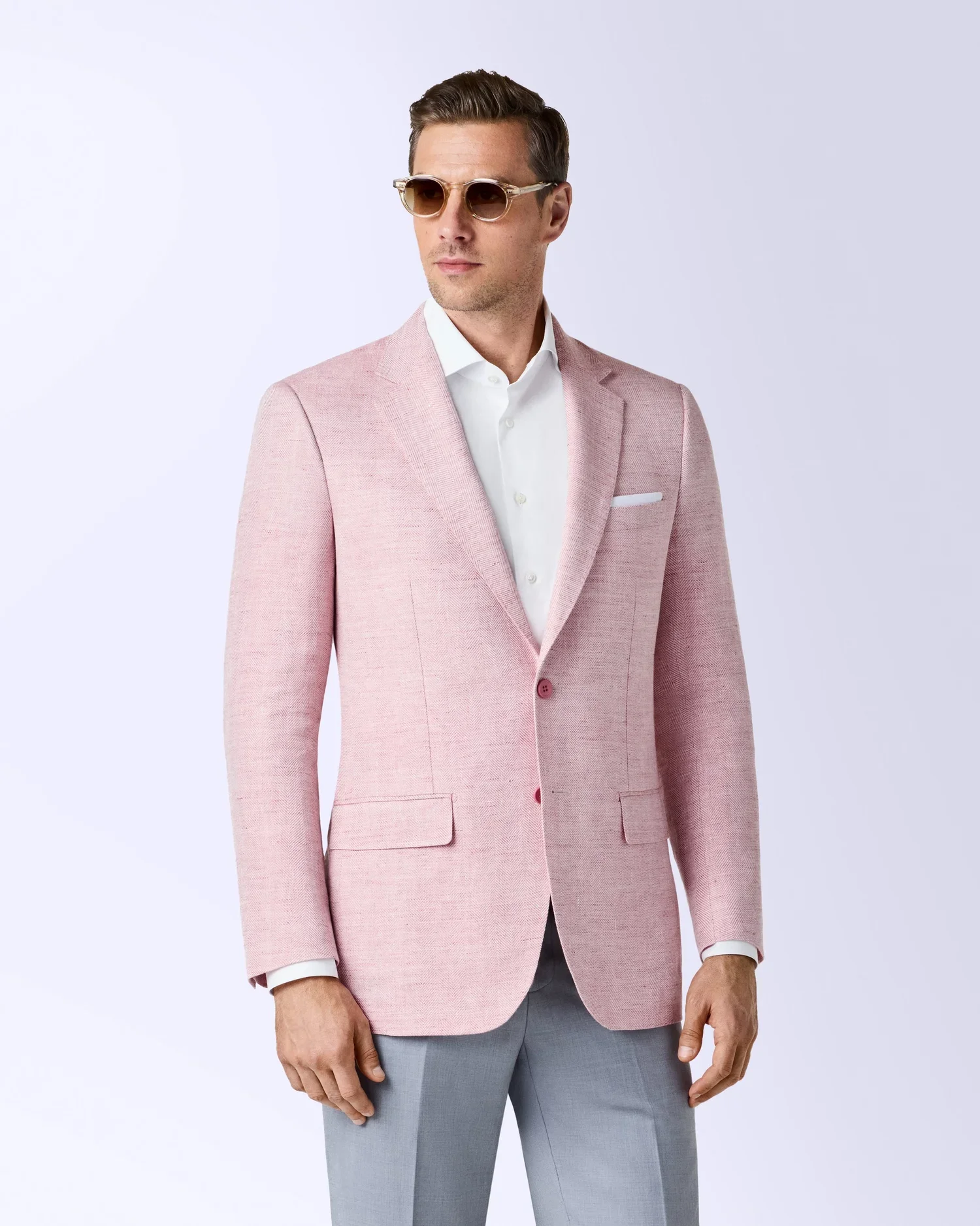 A man in a pink suit, white shirt, and sunglasses standing against a plain background.