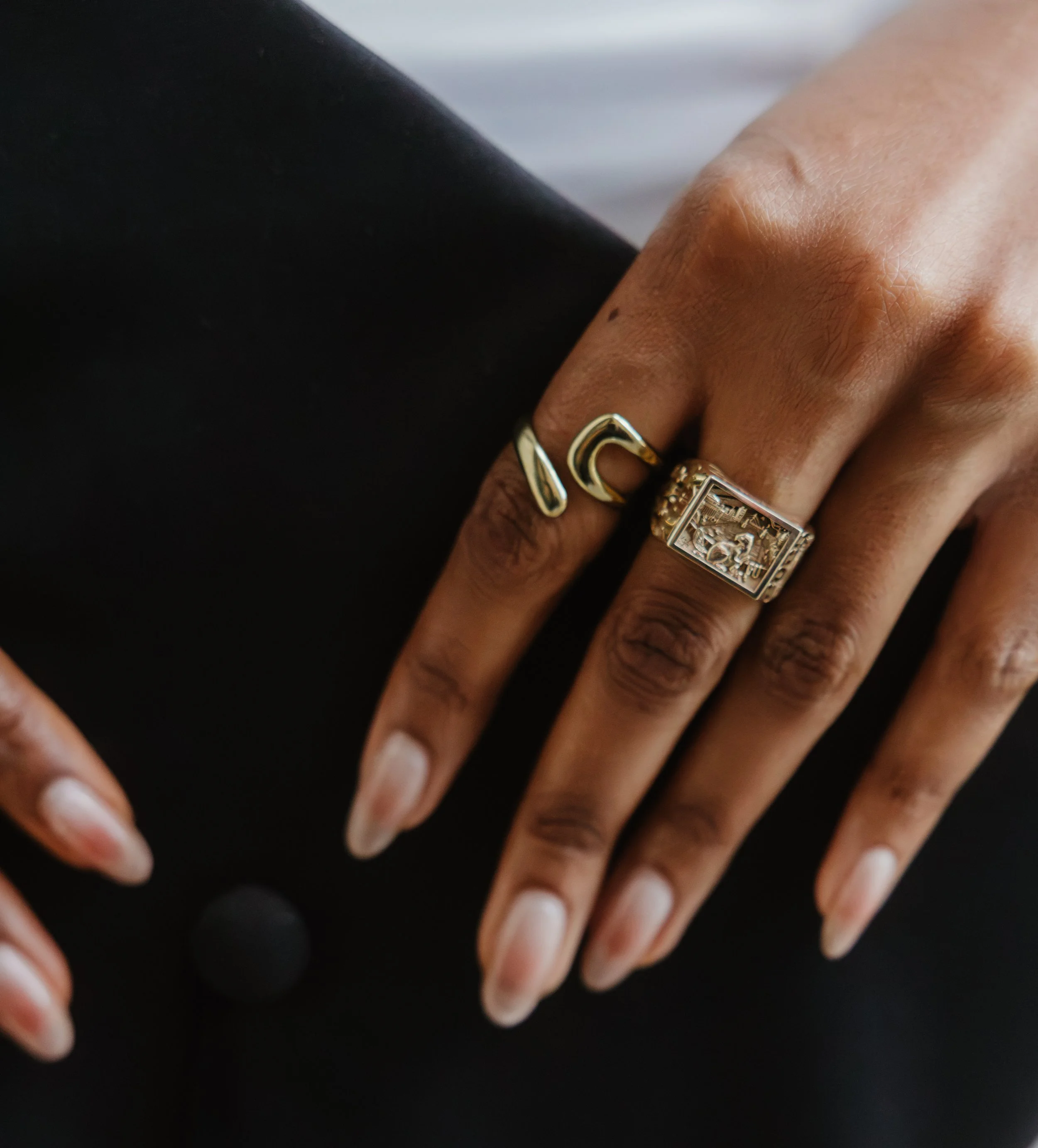 Close-up of four fingers with gold rings against a black background.