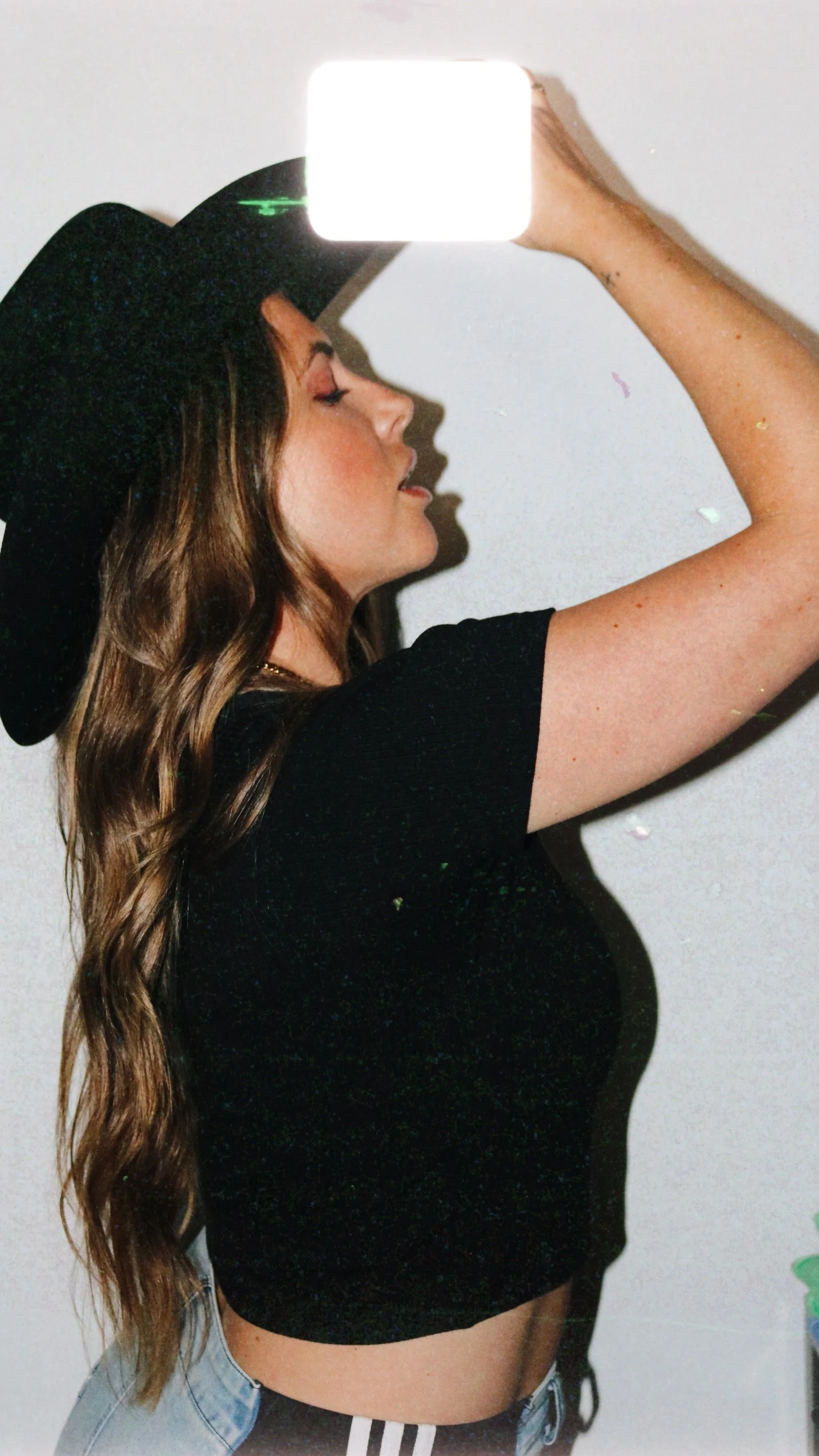 Woman with long wavy hair wearing a black hat, black crop top, and light blue jeans