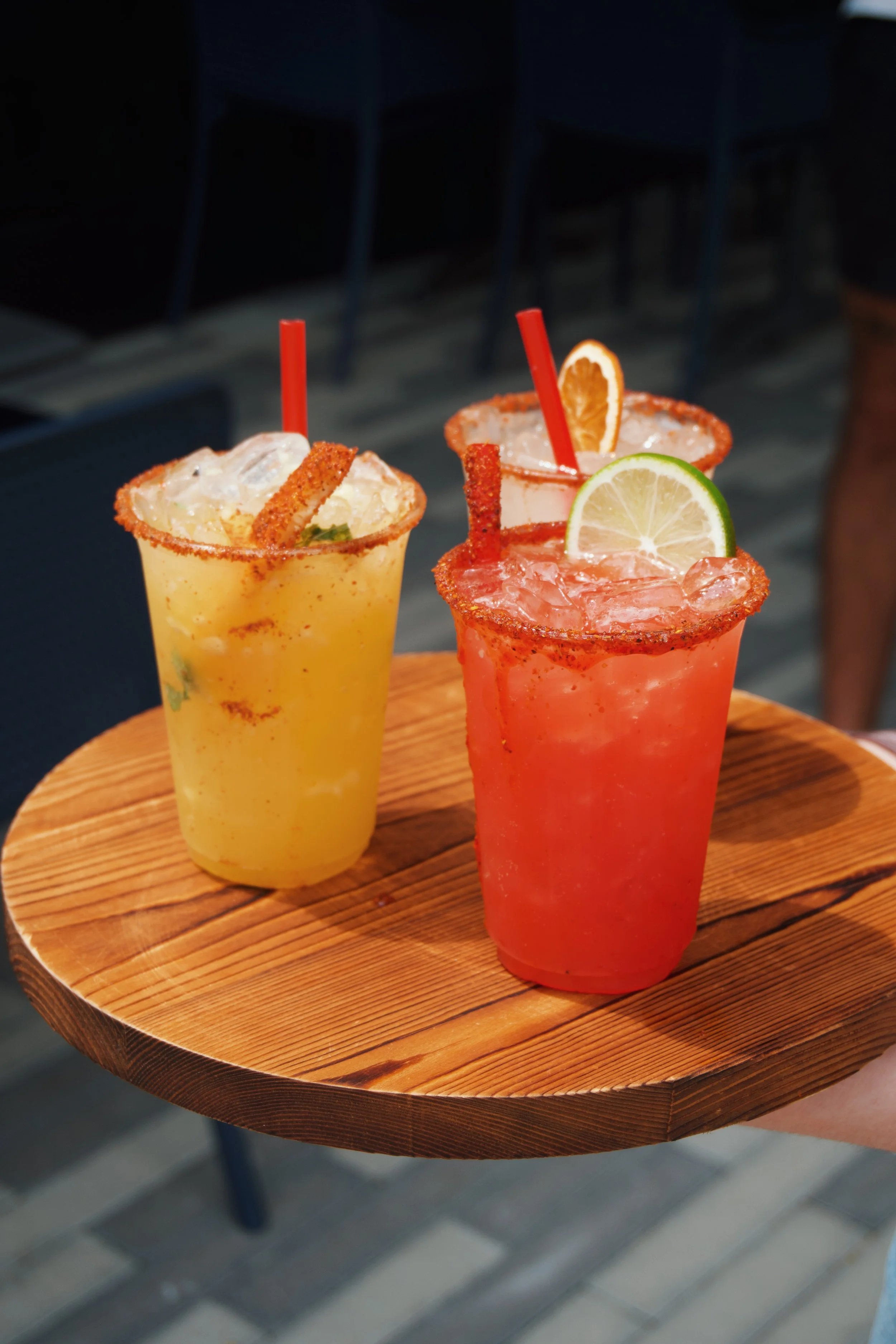 Two colorful cocktails with lime wedges and salted rims on a round wooden tray.