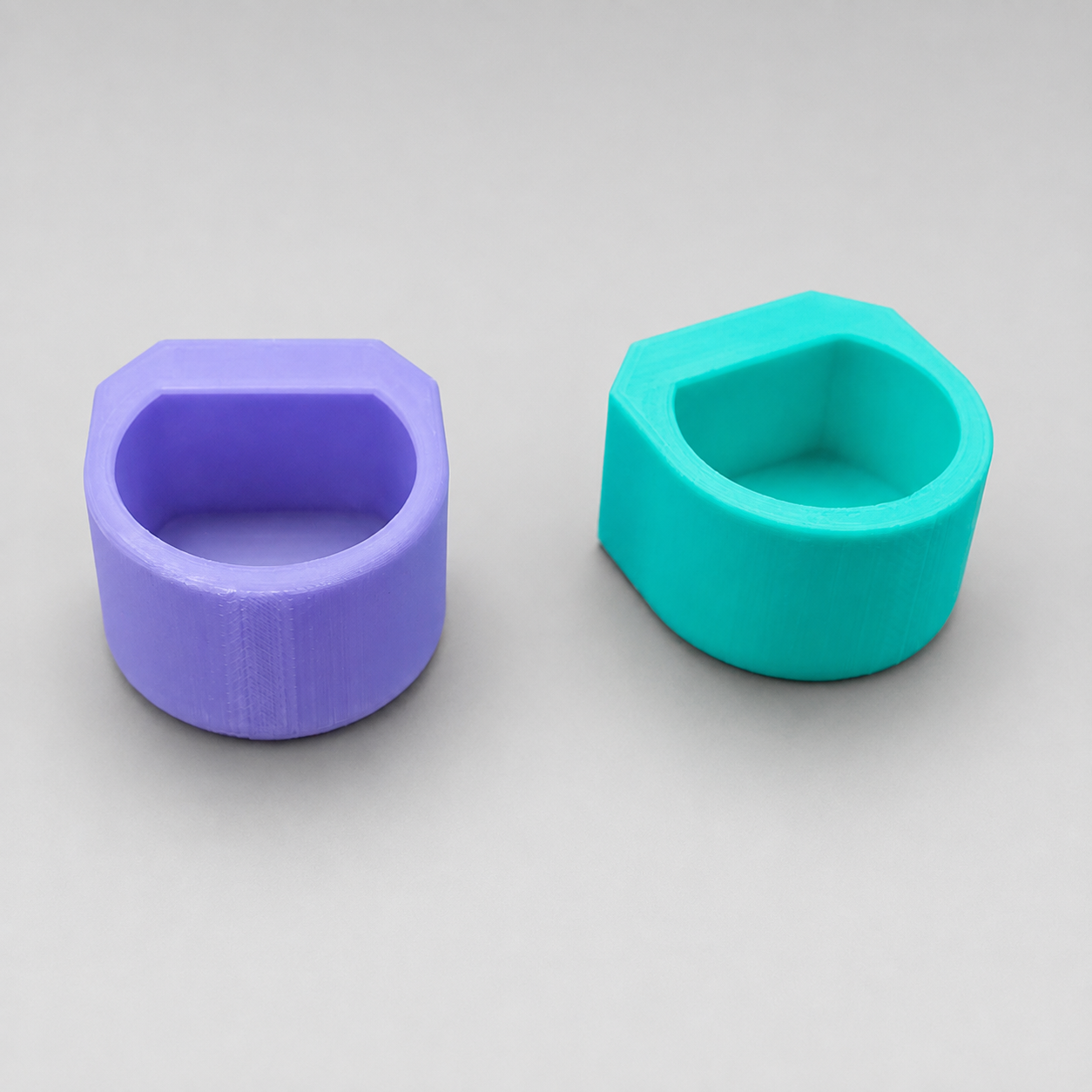 Front view of purple and teal Feeding Nooks, small 3D printed feeder dishes that can also be used as jumping spider hides.