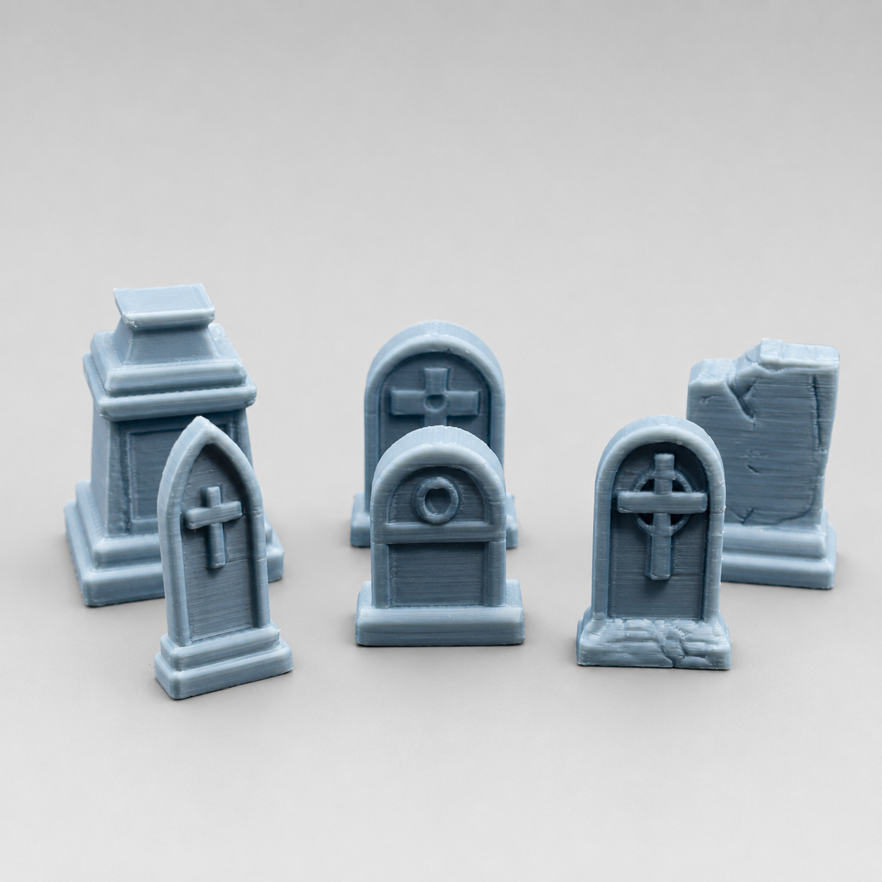 Six assorted miniature 3D printed grave markers and tombstones arranged as gothic jumping spider enclosure decor.