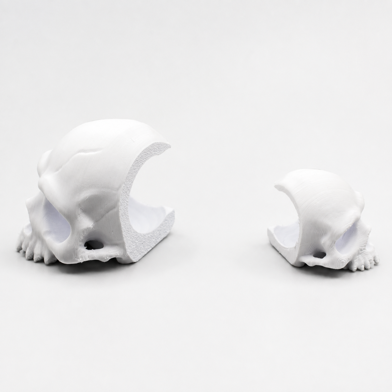 Side view of large and small 3D printed Corner Skull hides showing the cutaway peekaboo opening that sits against a clear jumping spider enclosure wall.