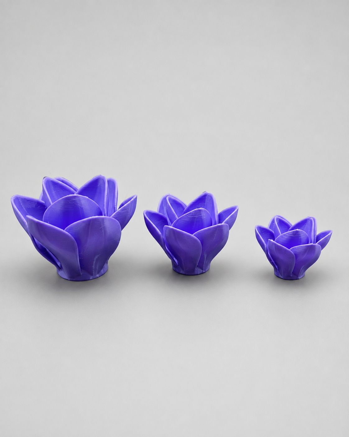 Top view of three purple 3D printed flower-shaped jumping spider hides showing layered petals and three available sizes.