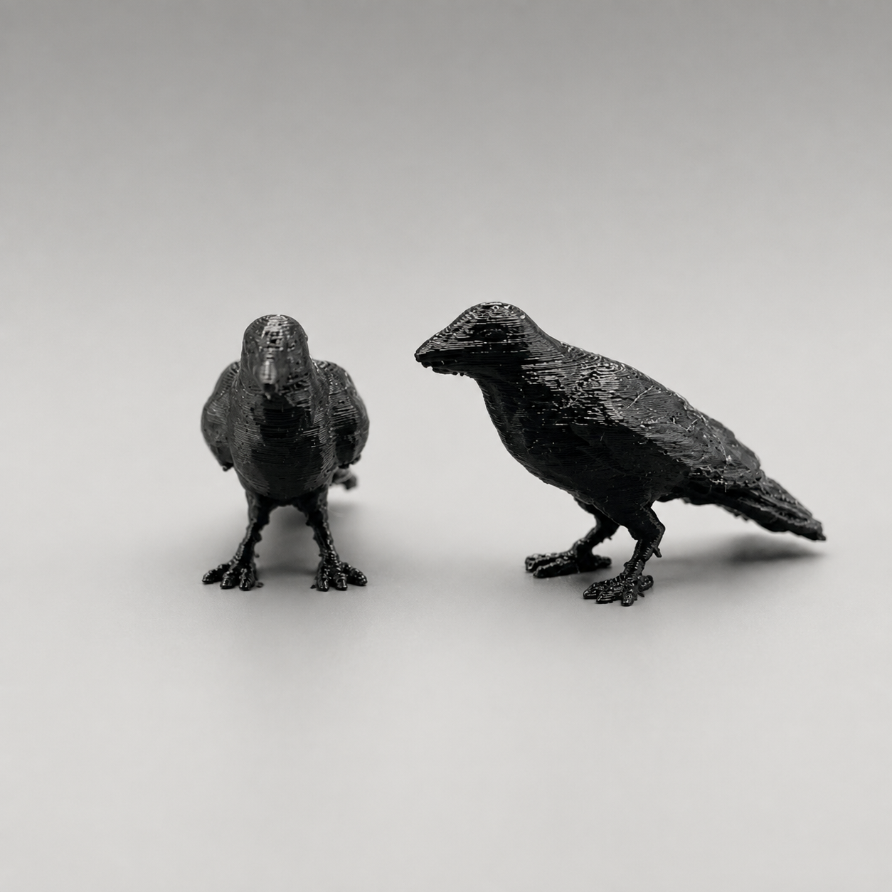 Set of two black 3D printed miniature crow figures, similar to ravens, in different poses for gothic jumping spider enclosure decor.