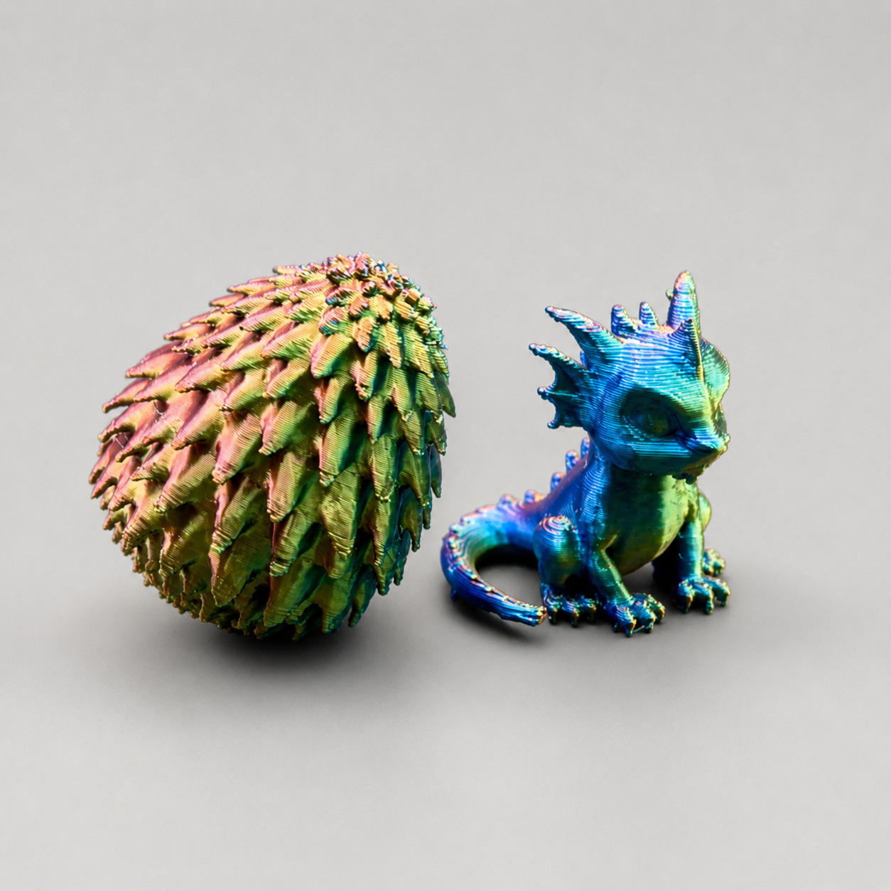 Side view of a miniature 3D printed dragon hatchling beside a textured dragon egg for jumping spider enclosure decor.