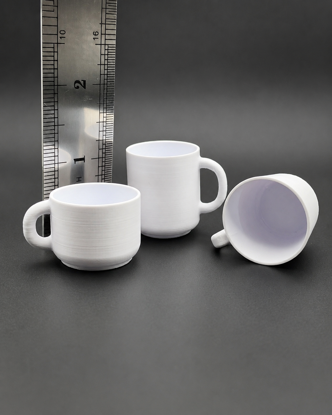 Three white 3D printed Cozy Cup Hides shown beside a ruler for size reference for jumping spider enclosures.