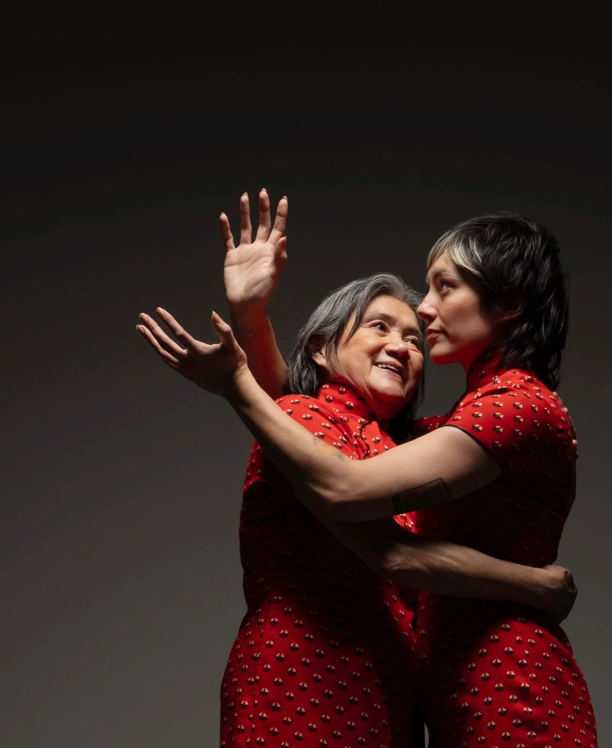 Melissa and Joy - a mother and daughter in matching red patterned qipao dresses - hug, with Melissa's hands stretched behind Joy's head in a gesture