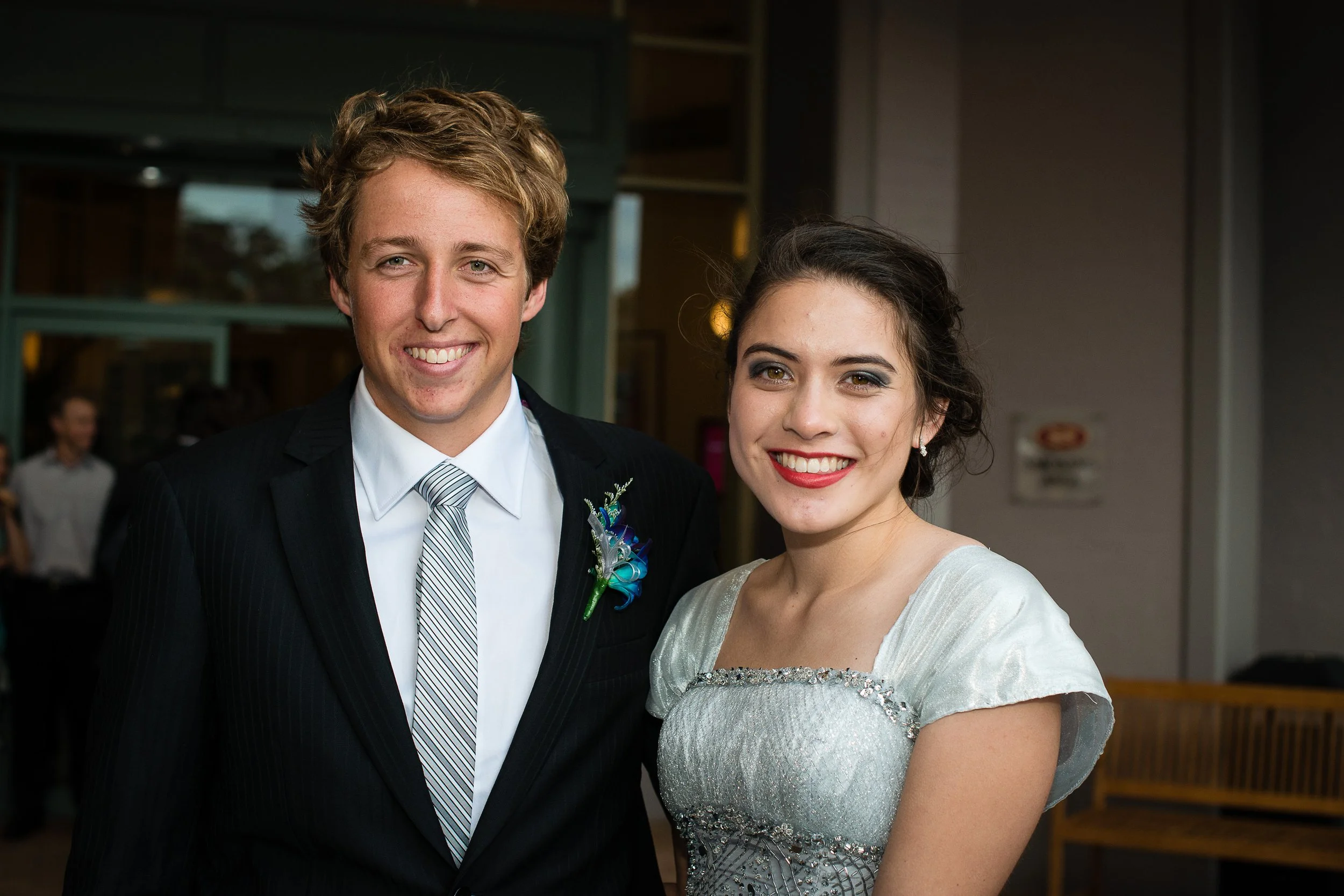 A young man and woman dressed in formal attire, smiling at the camera at a public event or celebration.