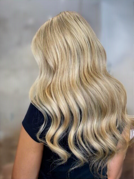 Back view of a woman with long, wavy blonde hair wearing a black shirt.