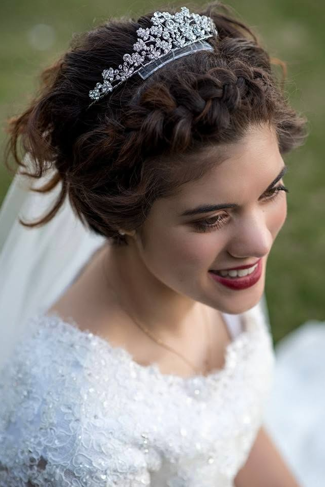 Close-up of a bride with dark curly hair wearing a sparkling tiara and a white wedding dress, outdoors.