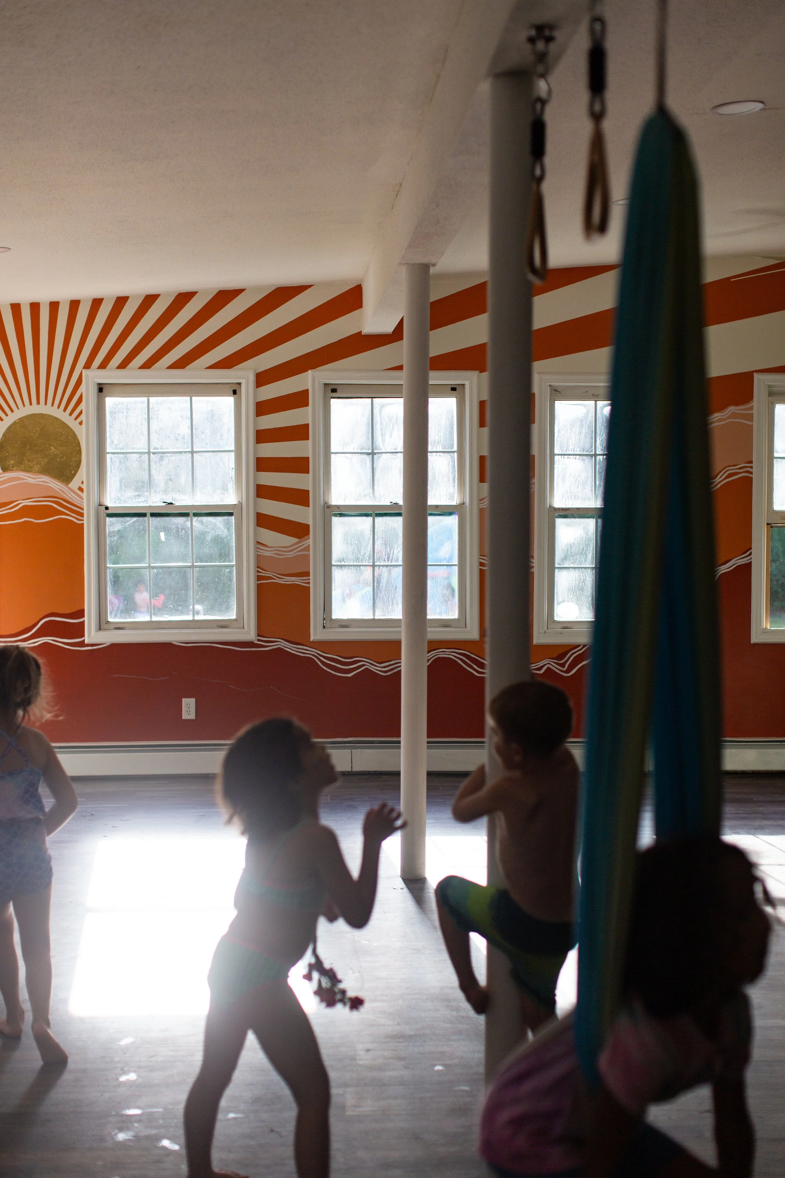 Children playing indoors in front of a sun and wave mural with windows and sunlight streaming in.