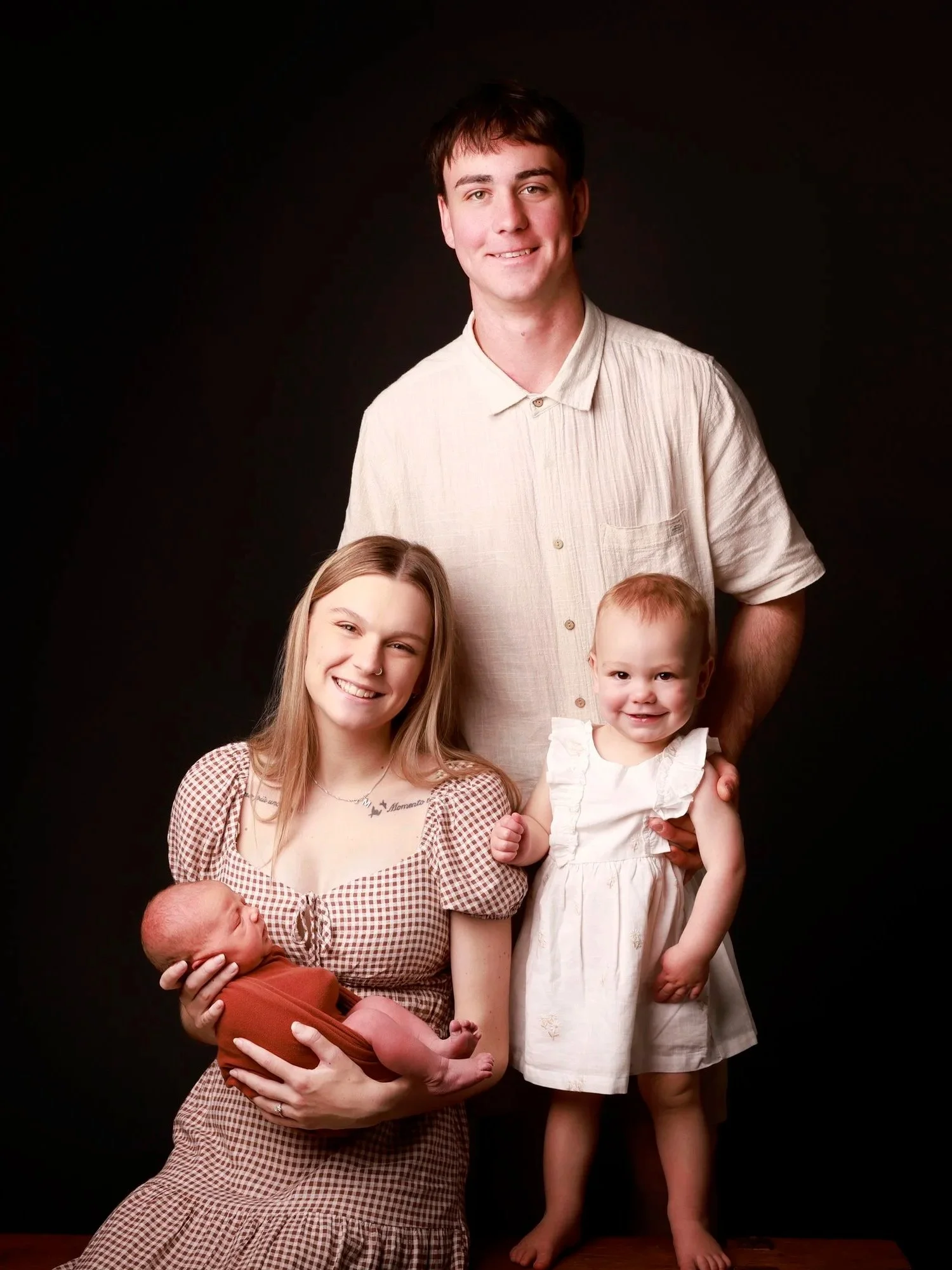 A family portrait of six members, including a man, woman, four children, and a newborn, standing against a black background.