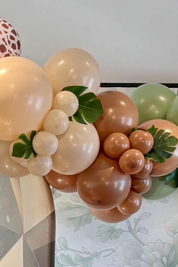 Decorative balloon arrangement with balloons in shades of cream, brown, and light green, accented with green leaves.