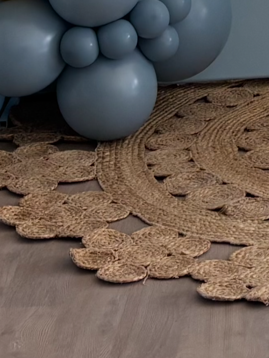 Part of a decorative arrangement that includes a cluster of light blue balloons and a round woven rug with a floral pattern.