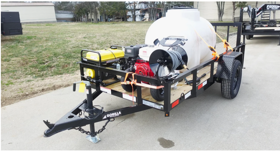 A black utility trailer with a white tank, yellow generator, and towing equipment, parked on a paved surface near grassy area.