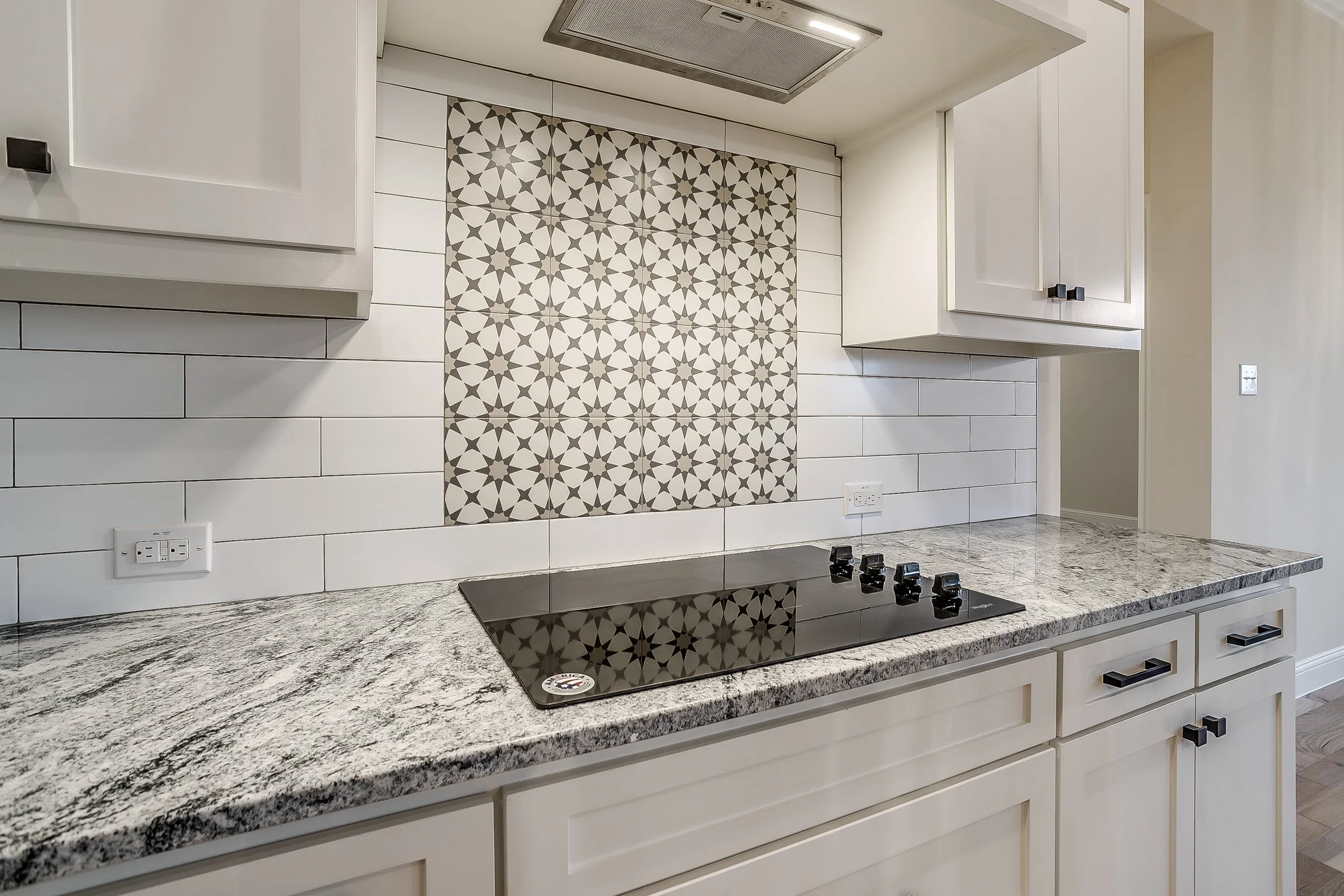 Modern kitchen with a granite countertop, white cabinets, a stove, and a decorative tile backsplash with a geometric star pattern.