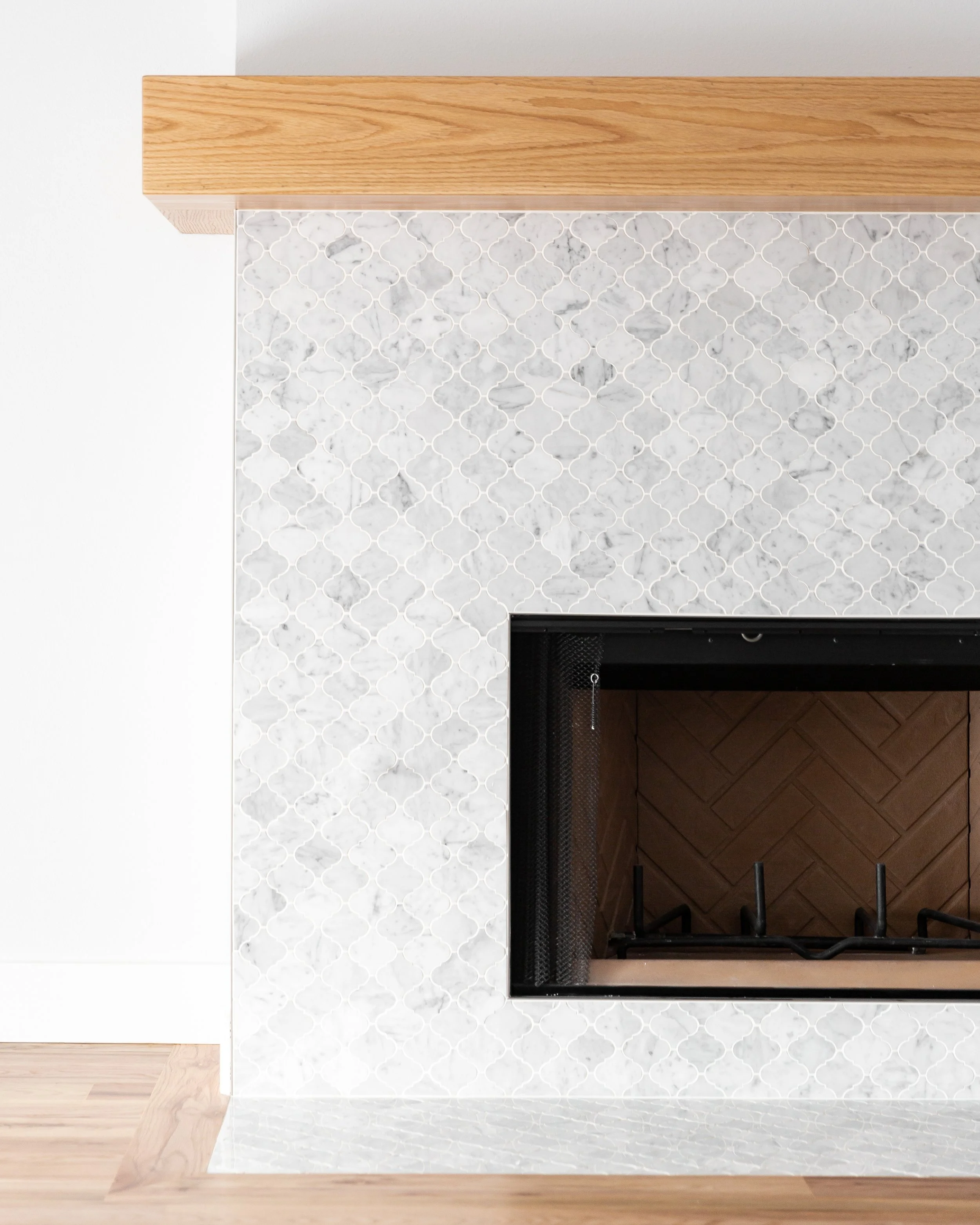 Top view of a kitchen island with a white marble countertop, a wooden edge, and a built-in black stove. The background shows wooden flooring, a white brick wall, and a white wall.