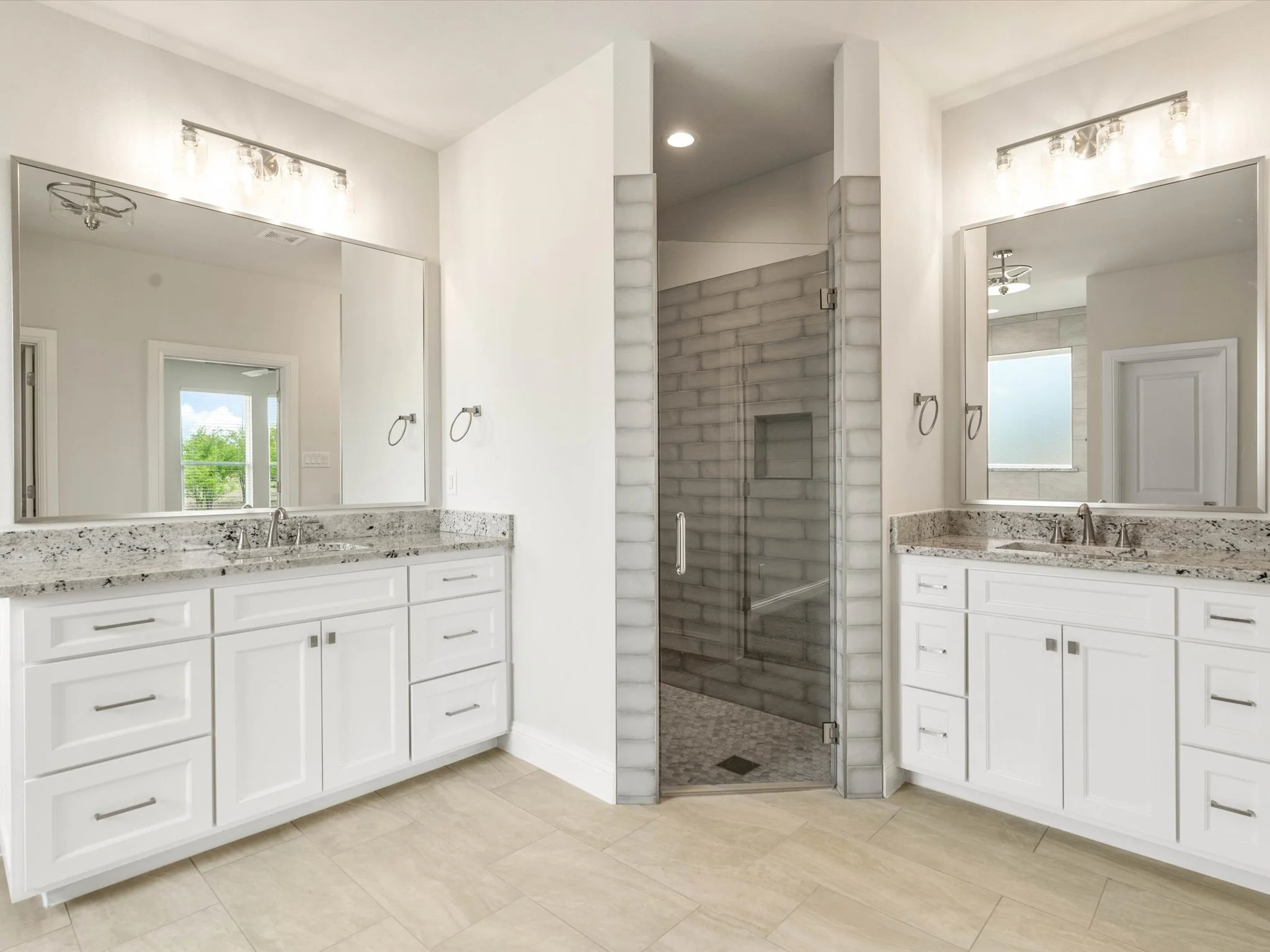 Modern bathroom with dual mirrors, granite countertops, and a walk-in shower with glass door and brick tile walls.