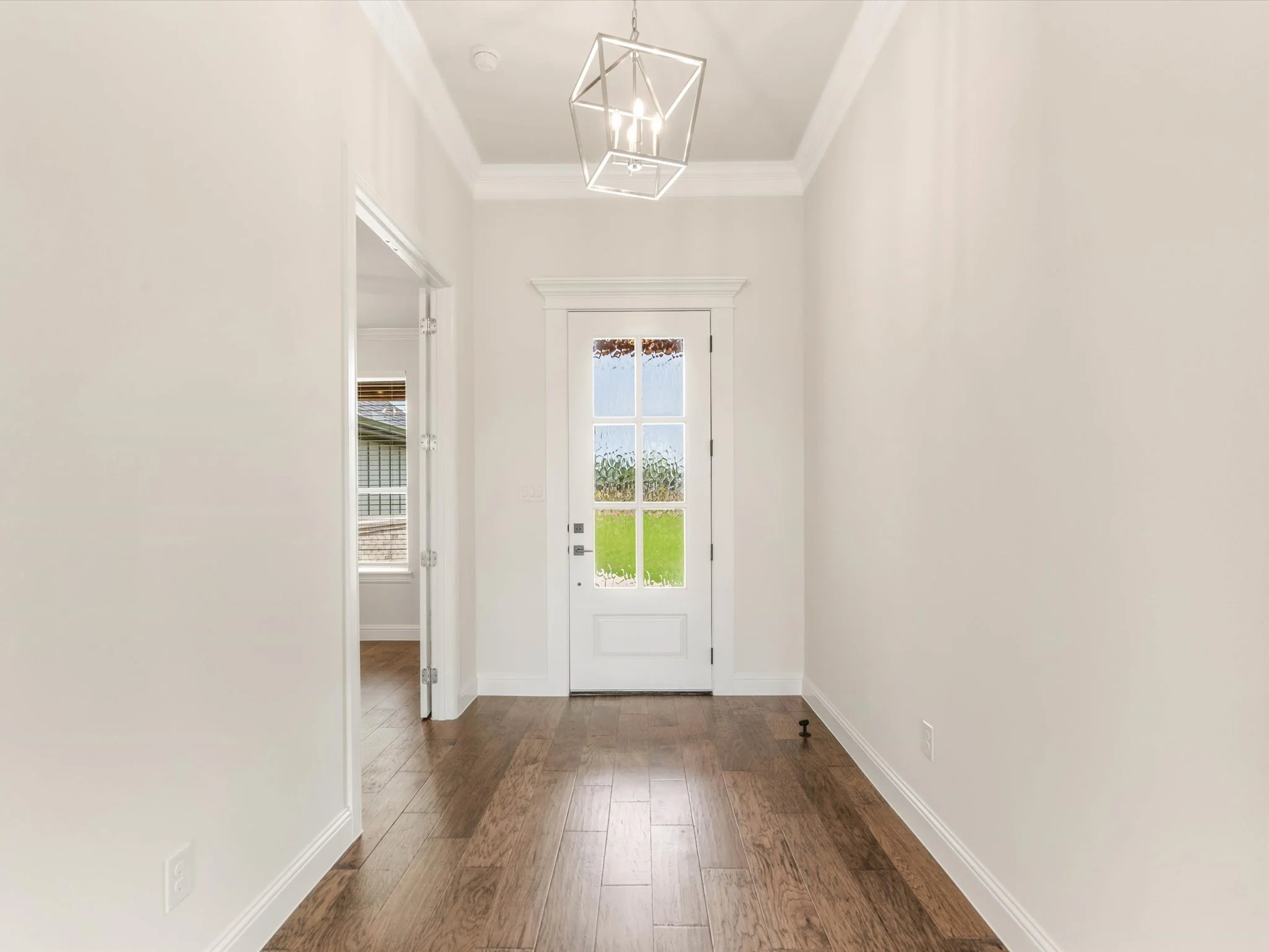 Entryway with white walls, wooden flooring, a modern geometric chandelier, and a glass-paned door leading outside.