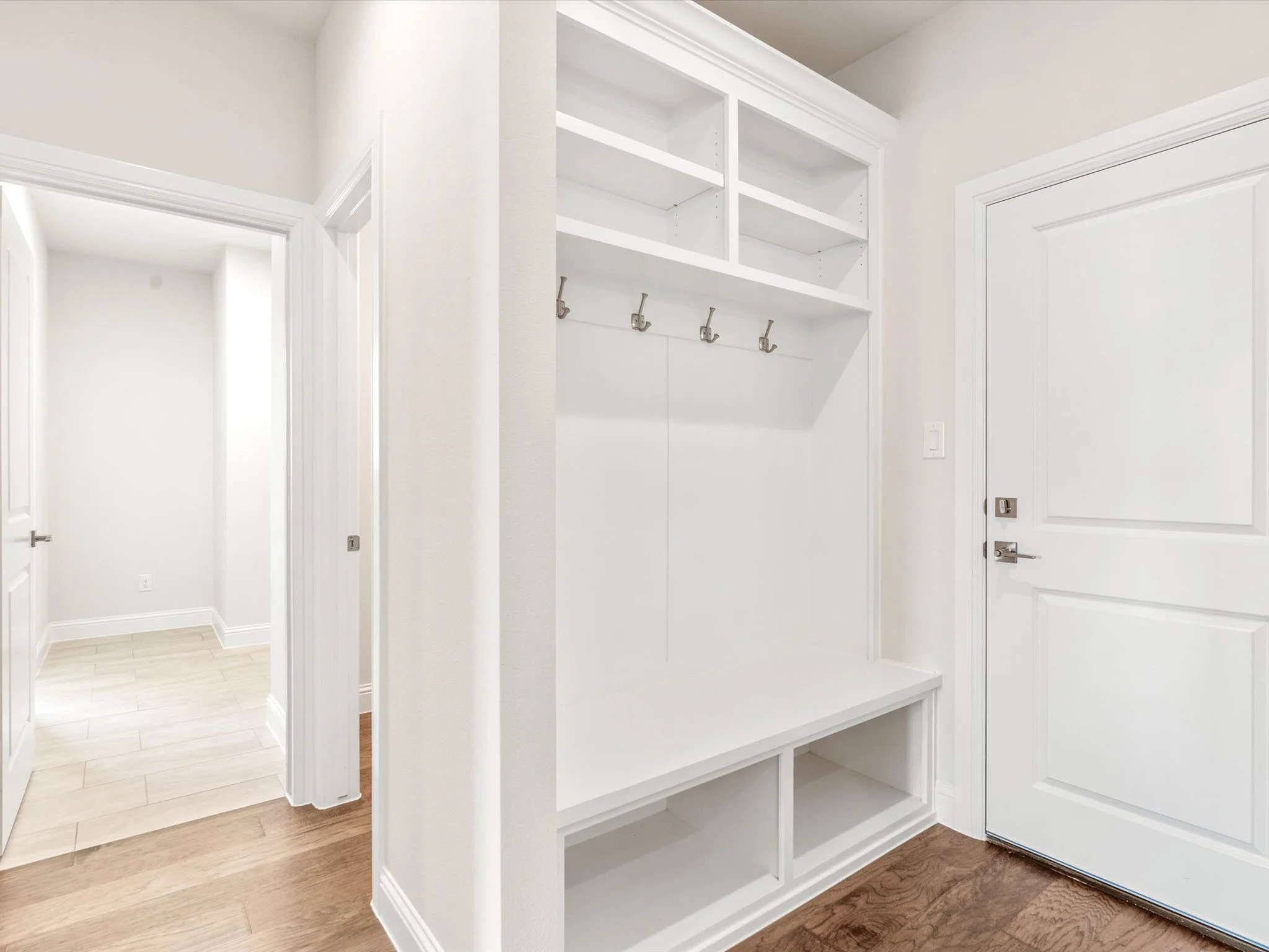Empty white built-in shelves with hooks underneath in a doorway alcove of a home interior.