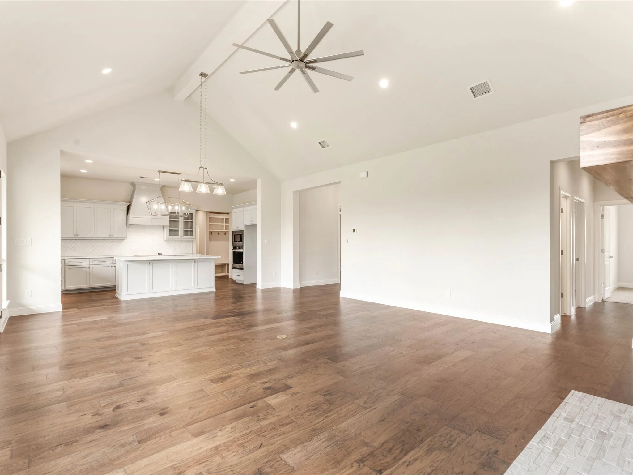 Open-concept living space with hardwood floors, white walls, a ceiling fan, recessed lighting, and a view of a kitchen with white cabinets and countertops.