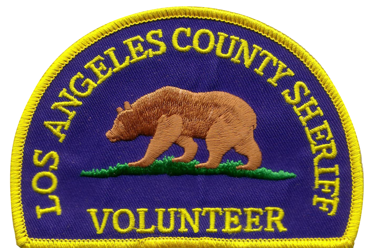 An embroidered patch with purple background and yellow border. It features a brown bear walking on green grass, with yellow text that reads 'LOS ANGELES COUNTY SHERIFF VOLUNTEER' around the bear.