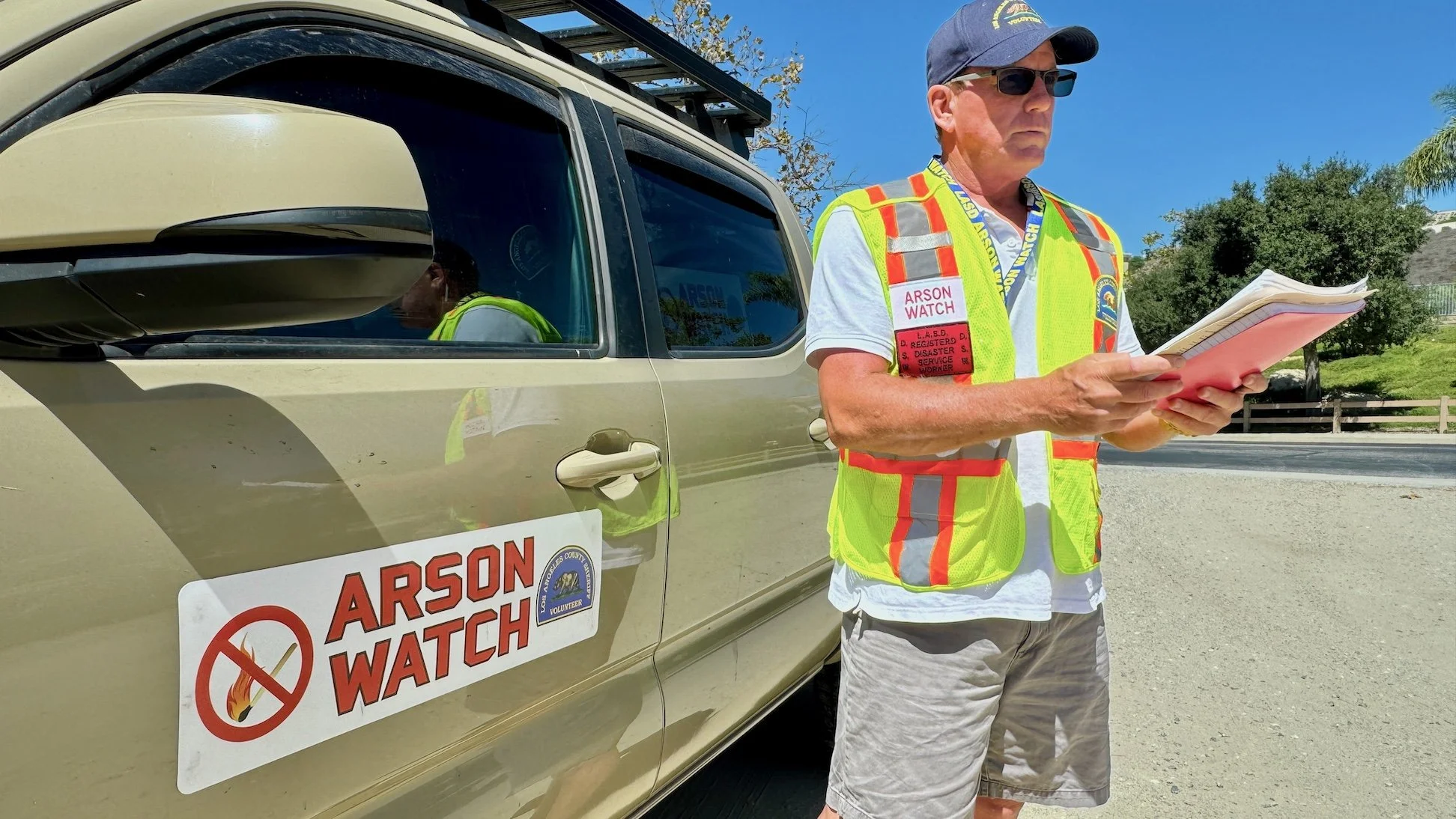 Arson Watch member standing next to his car with an Arson Watch sign and looking at his the Arson Watch field guide