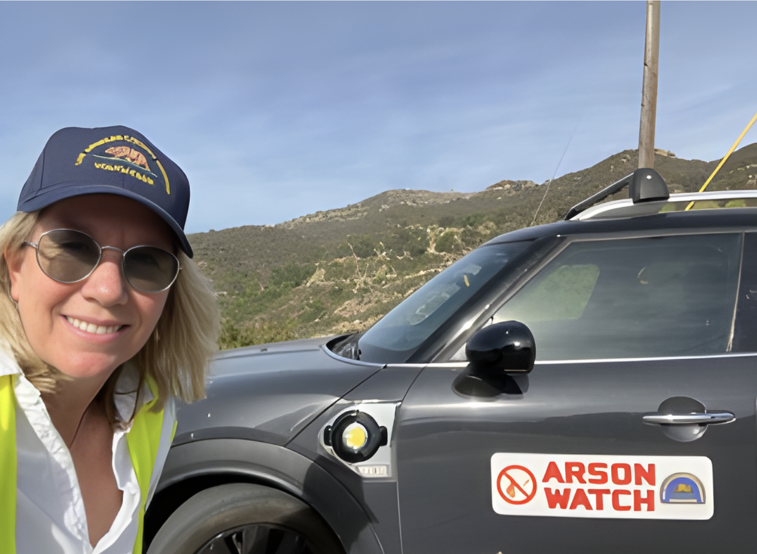 Arson Watch volunteer in gear on patrol, standing next to her vehicle with ‘rson Watch signage