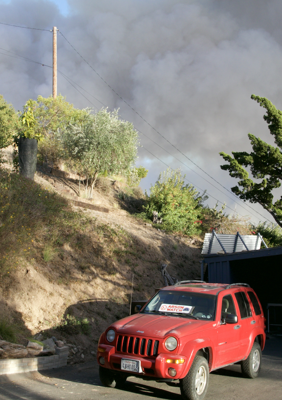 Red Jeep with Arson Watch signage parked with thick wildfire smoke on the horizon